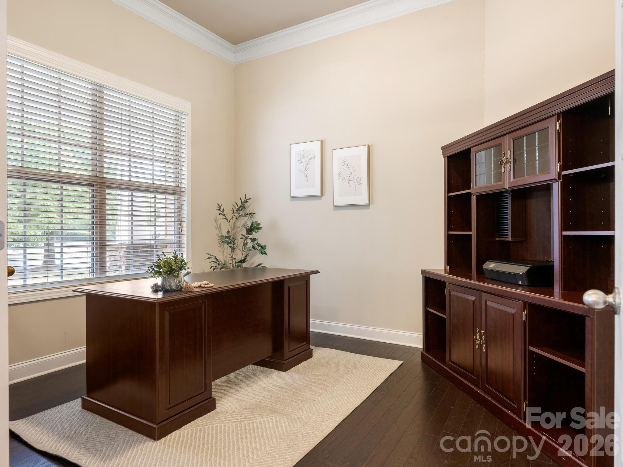 Furnished home office with a dark wood desk, matching cabinetry, and a large window with blinds.