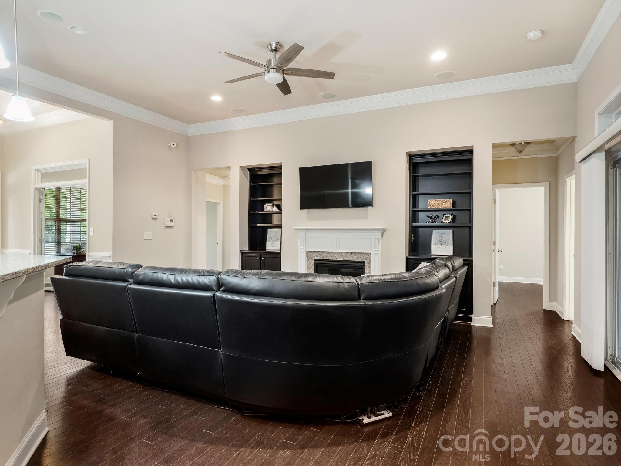 Living room with a black sectional, fireplace, wall-mounted TV, and built-in bookshelves.