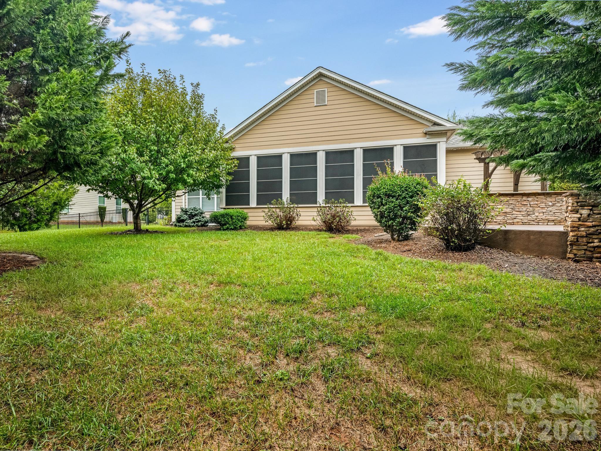 Tan house with a large screened porch behind a grassy backyard and mature landscaping.