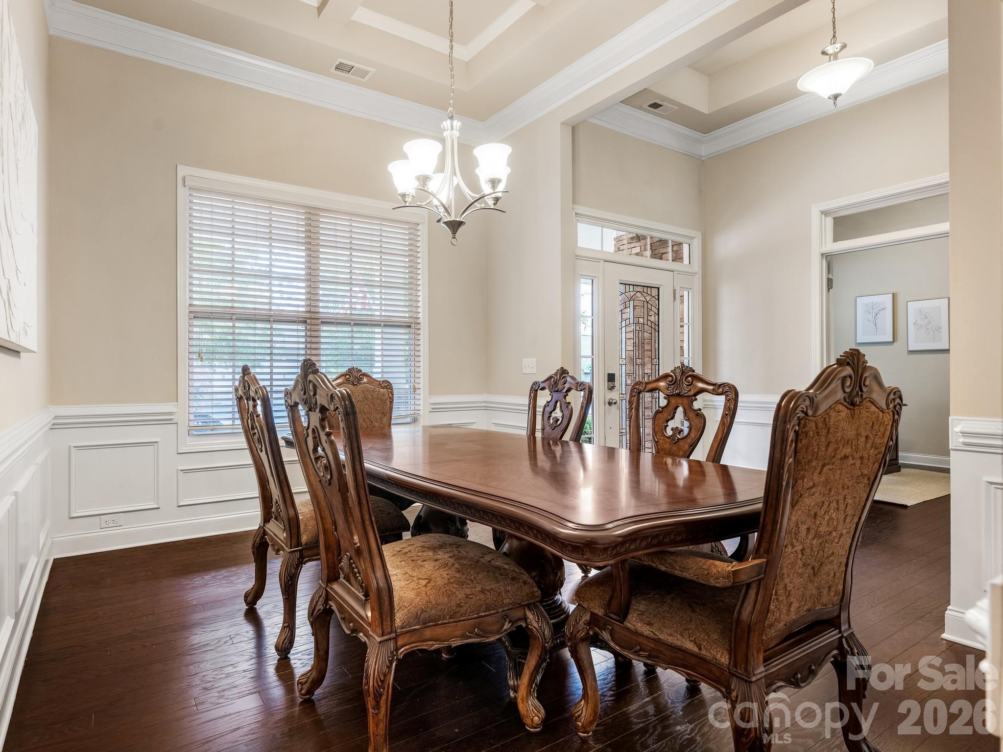 Furnished dining room with an ornate dark wood table, carved chairs, hardwood floors, and a tray ceiling.