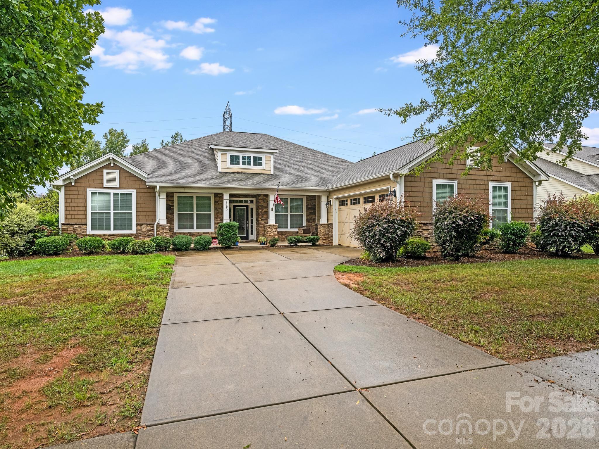 Single-story home with stone accents, attached garage, landscaped yard, and wide concrete driveway.