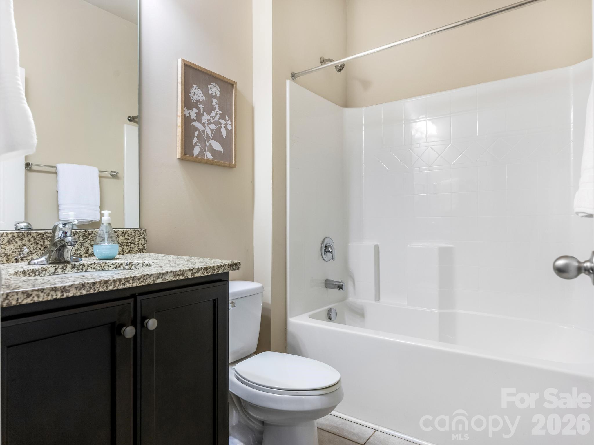 Bathroom with white tiled tub and shower beside a dark vanity with granite countertop.