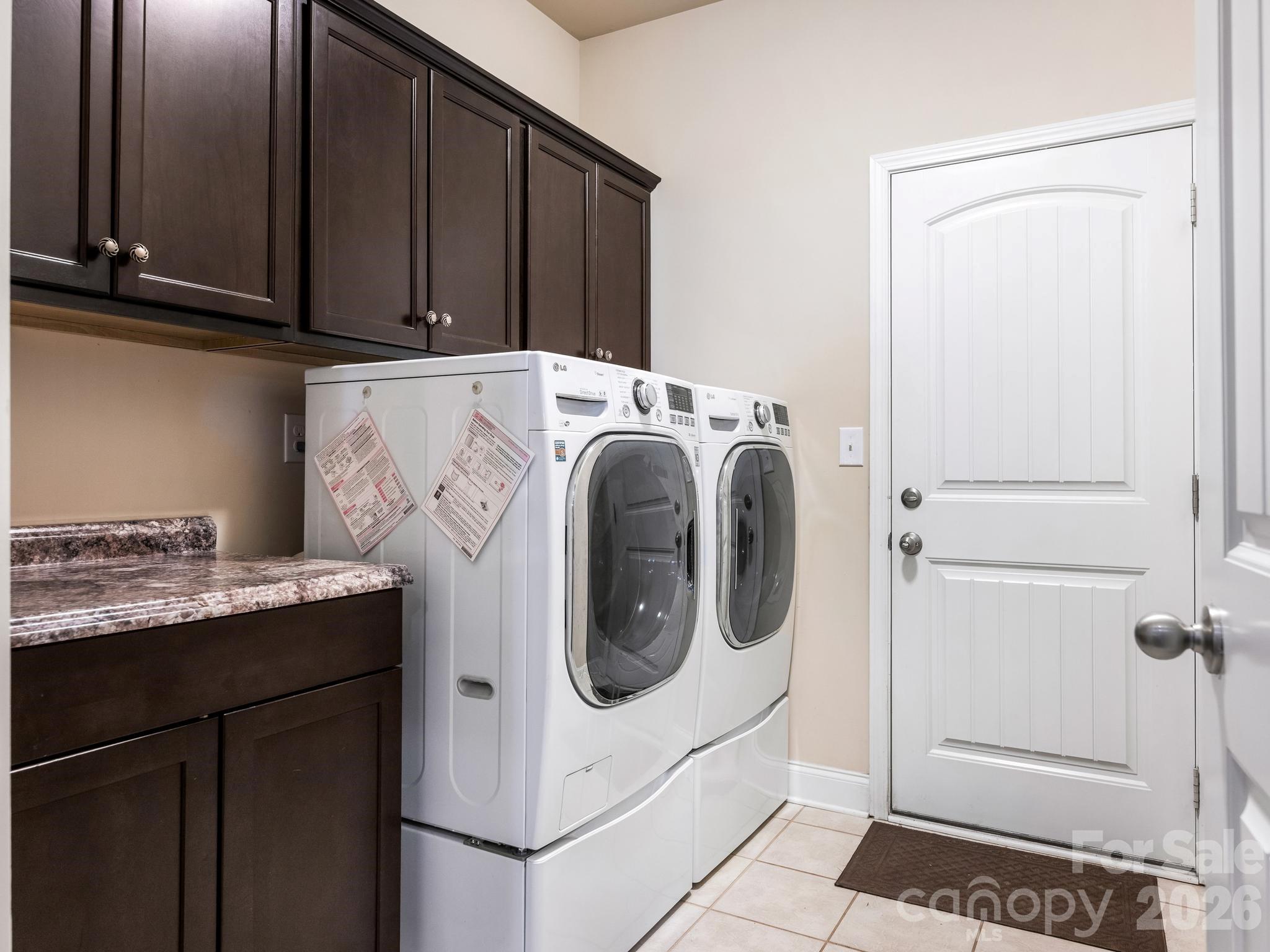 Laundry room with front-loading washer and dryer, dark cabinets, and granite countertop.
