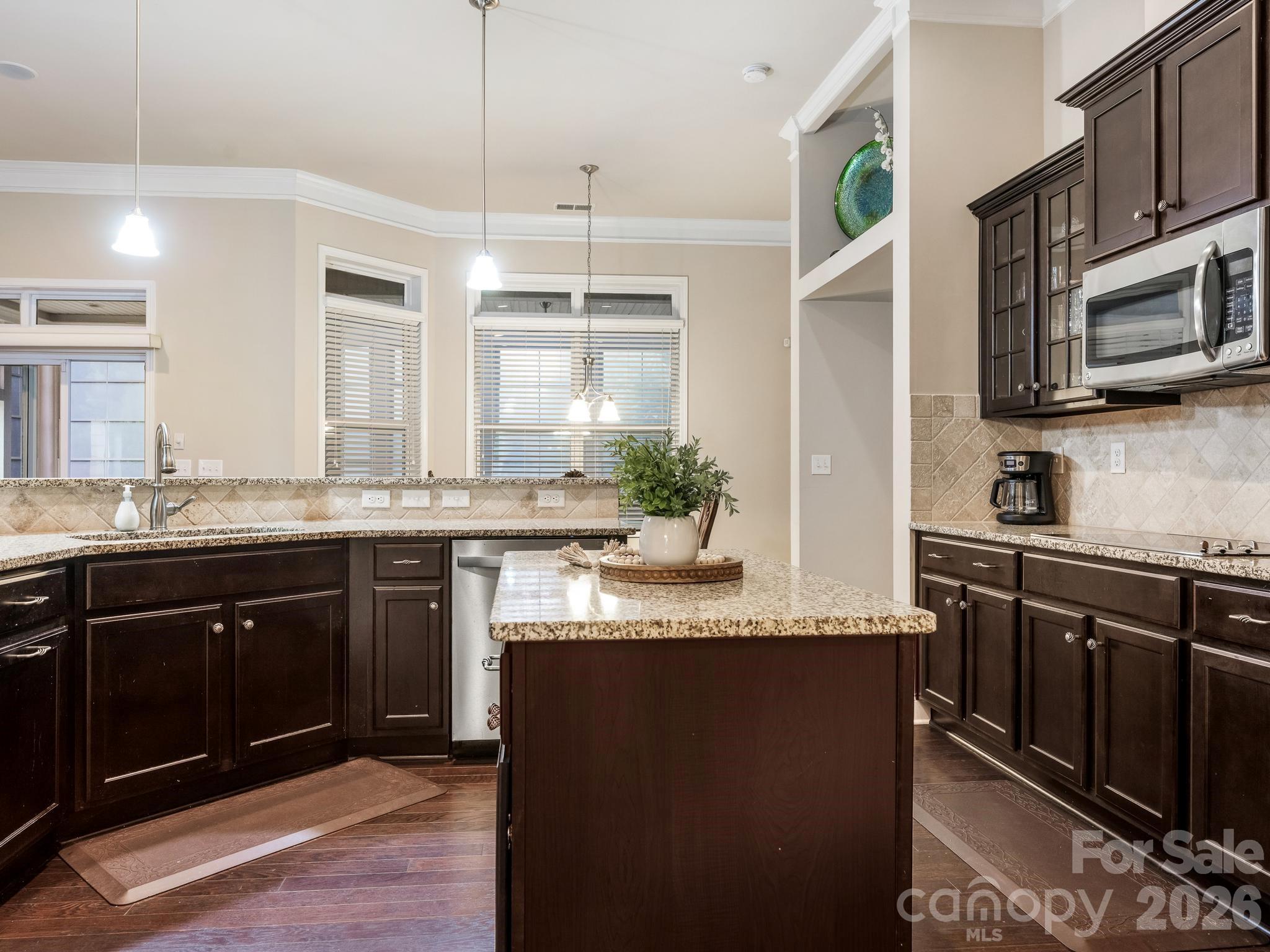 Kitchen with dark wood cabinets, granite island, stainless steel appliances, and large windows.