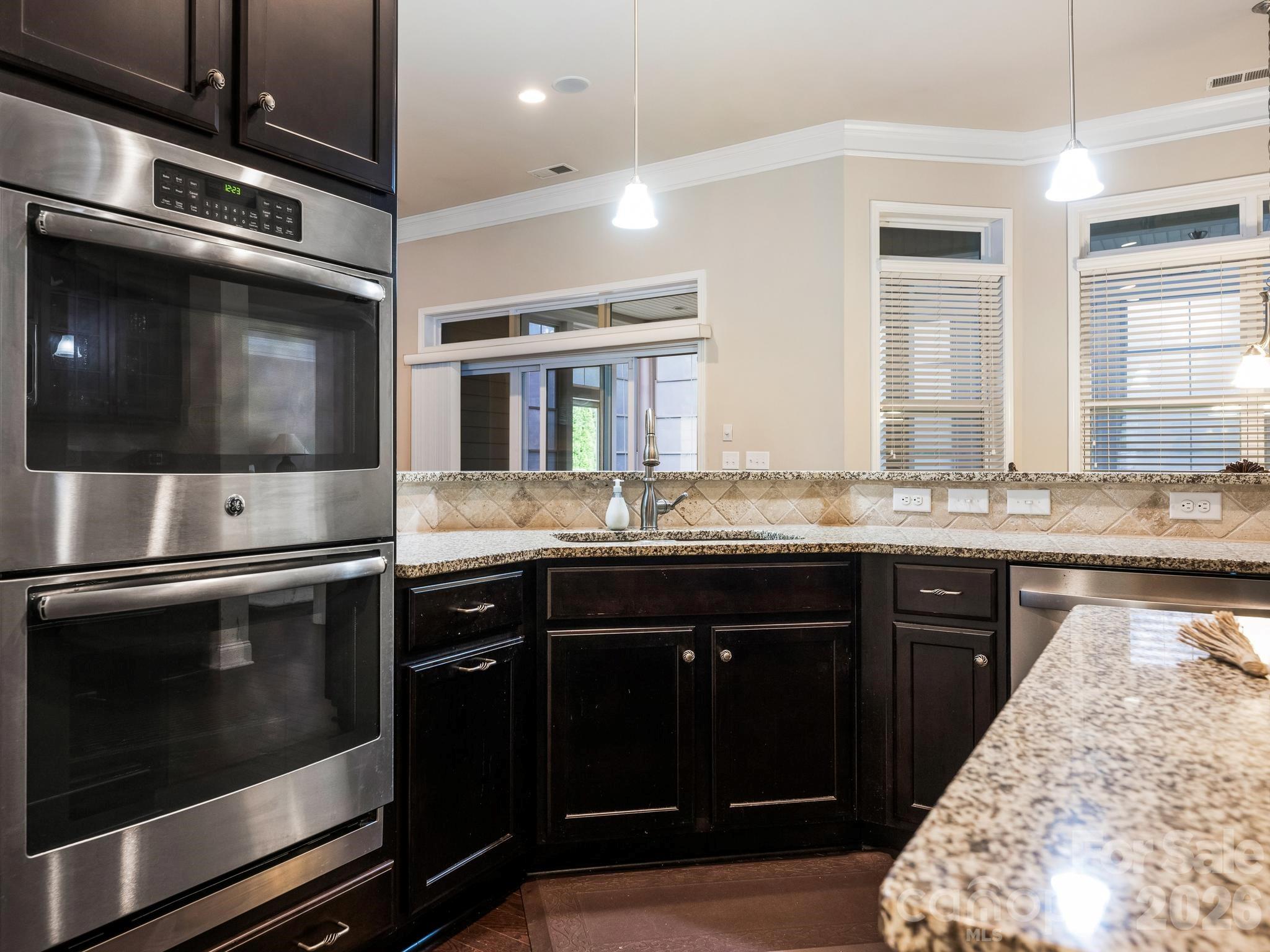 Kitchen with dark cabinets, stainless steel double ovens, granite counters, and windows with blinds.