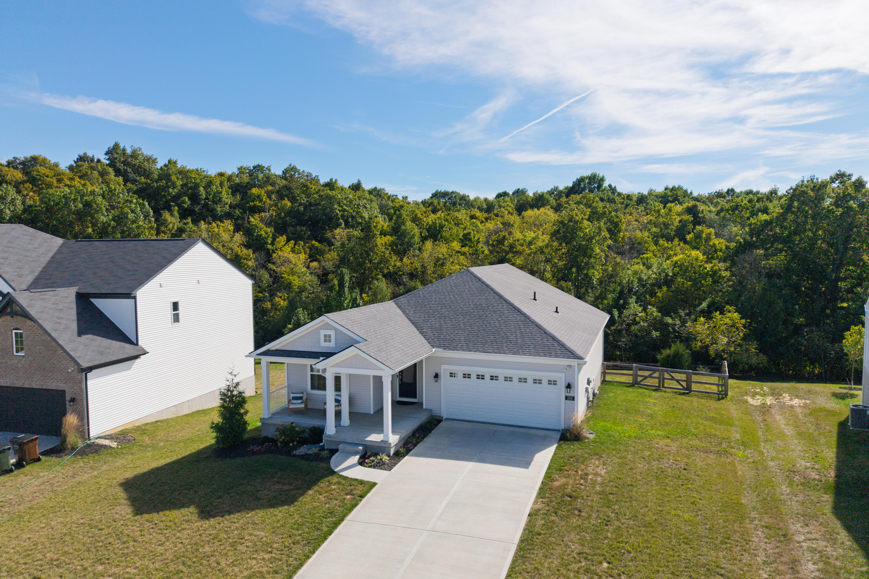 Aerial view of a white home with a covered porch, two-car garage, and wooded backdrop.