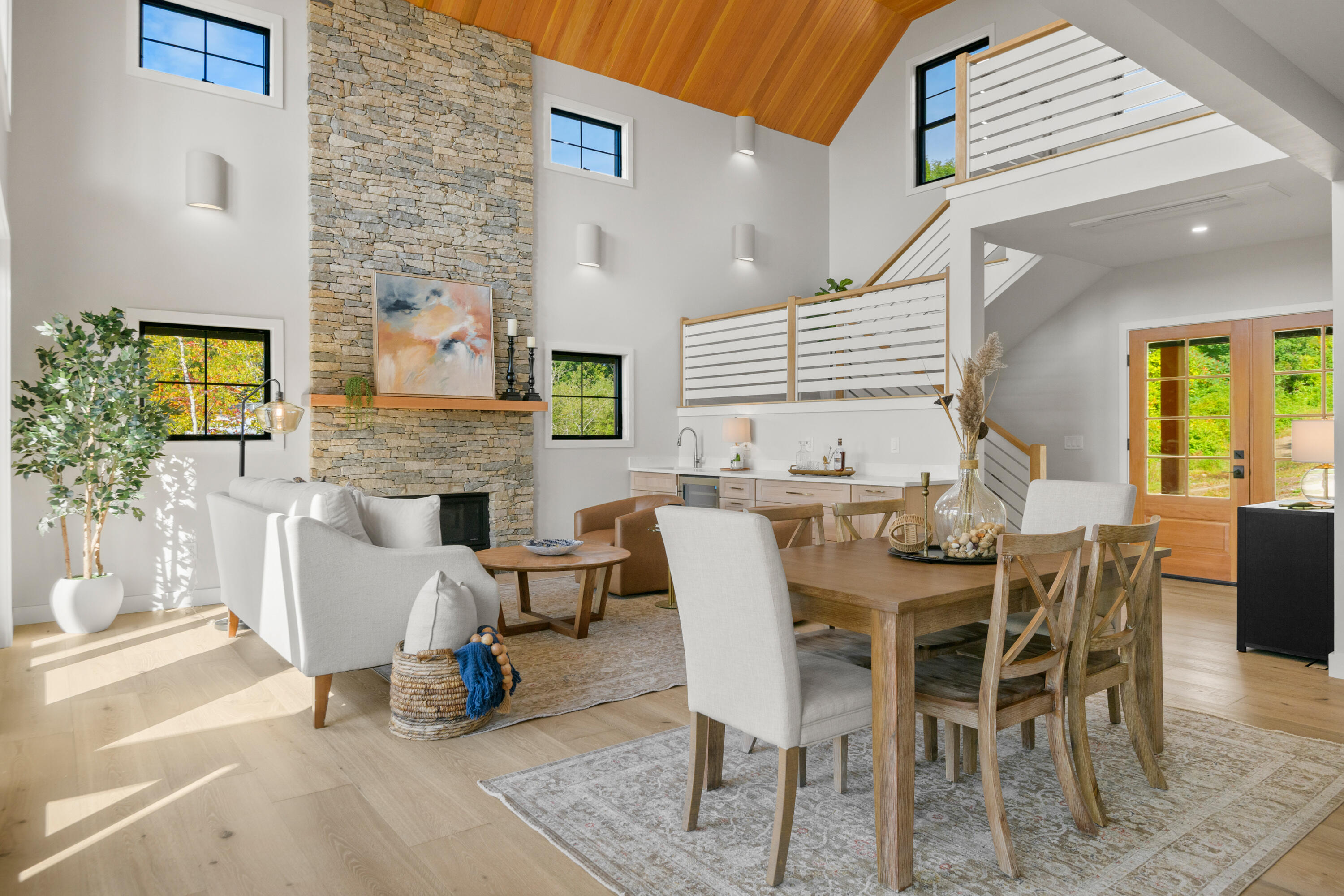 Open-plan living and dining room with a vaulted wood ceiling and tall stone fireplace.