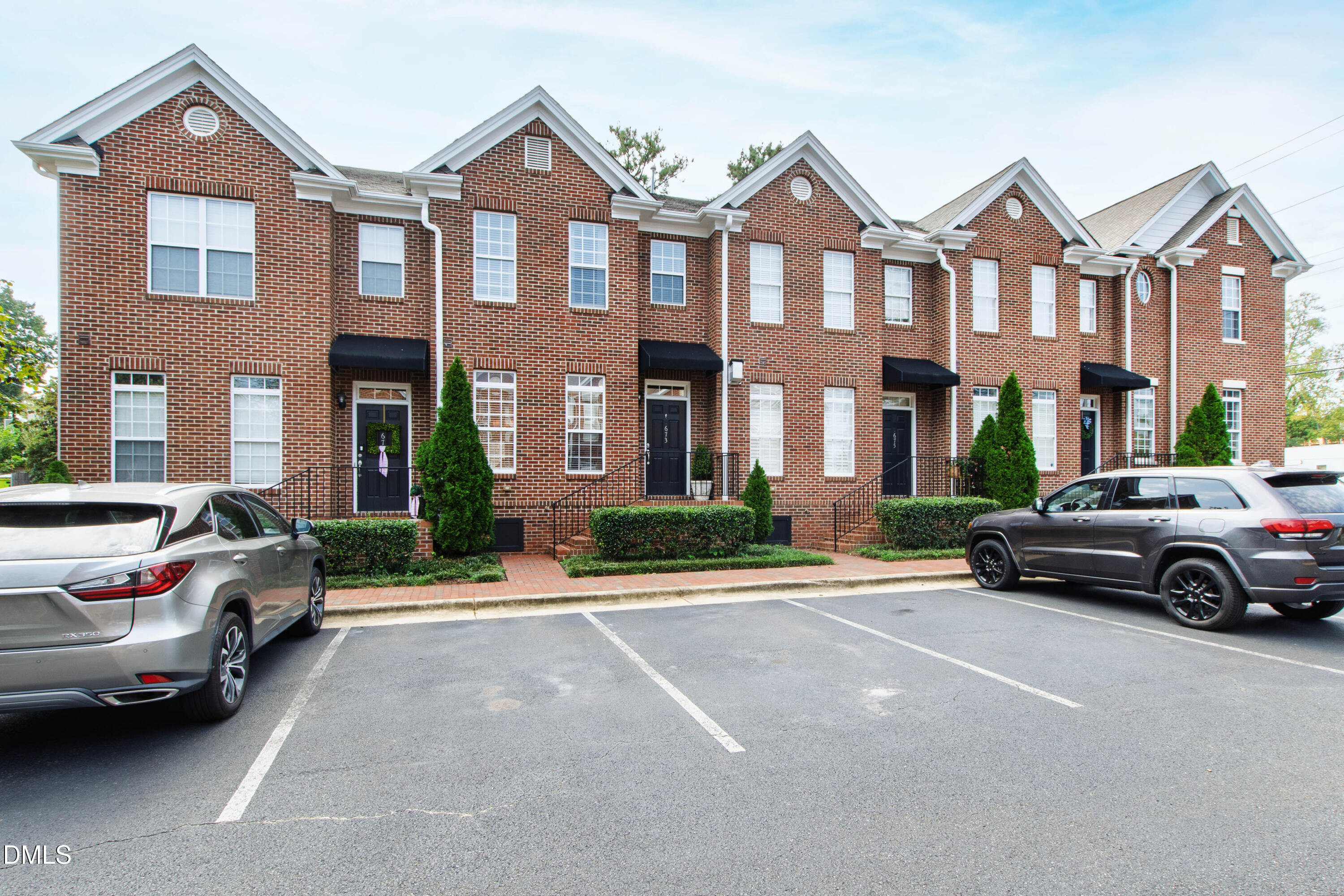 Red-brick townhomes with black entry awnings and parked cars in front.
