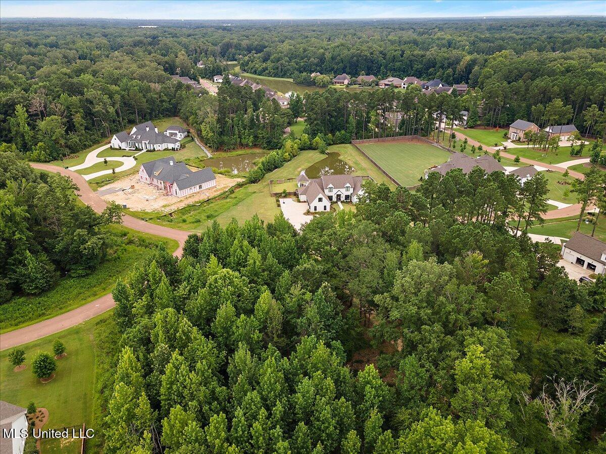 Aerial view of a wooded neighborhood with homes, ponds, and a fenced sports court.