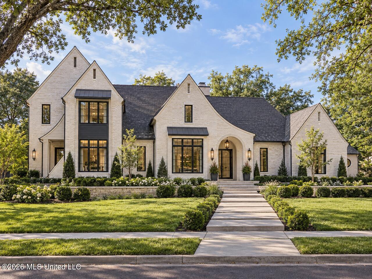 Light-brick home with multiple gables, an arched entry, and a stone walkway through landscaped gardens.