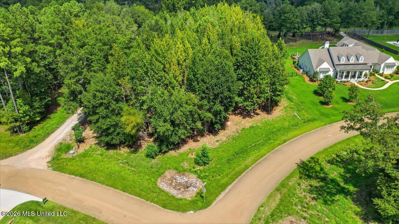 Aerial view of a wooded vacant lot at a road corner beside a large home.