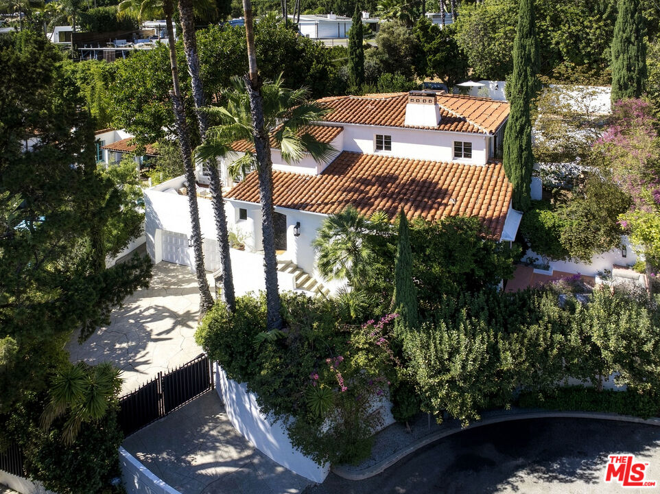 White two-story home with terracotta tile roofs, a gated driveway, and mature landscaping, seen from above.