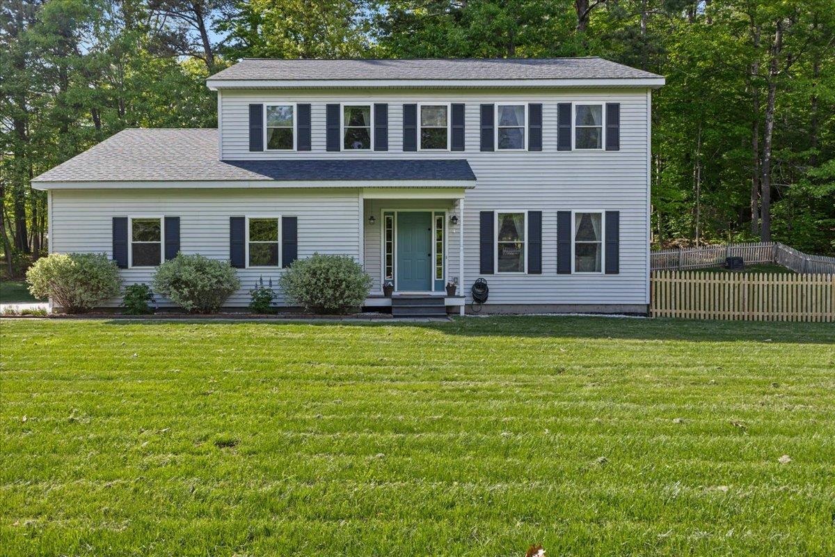 Two-story white house with dark shutters, a green front door, and a broad lawn.