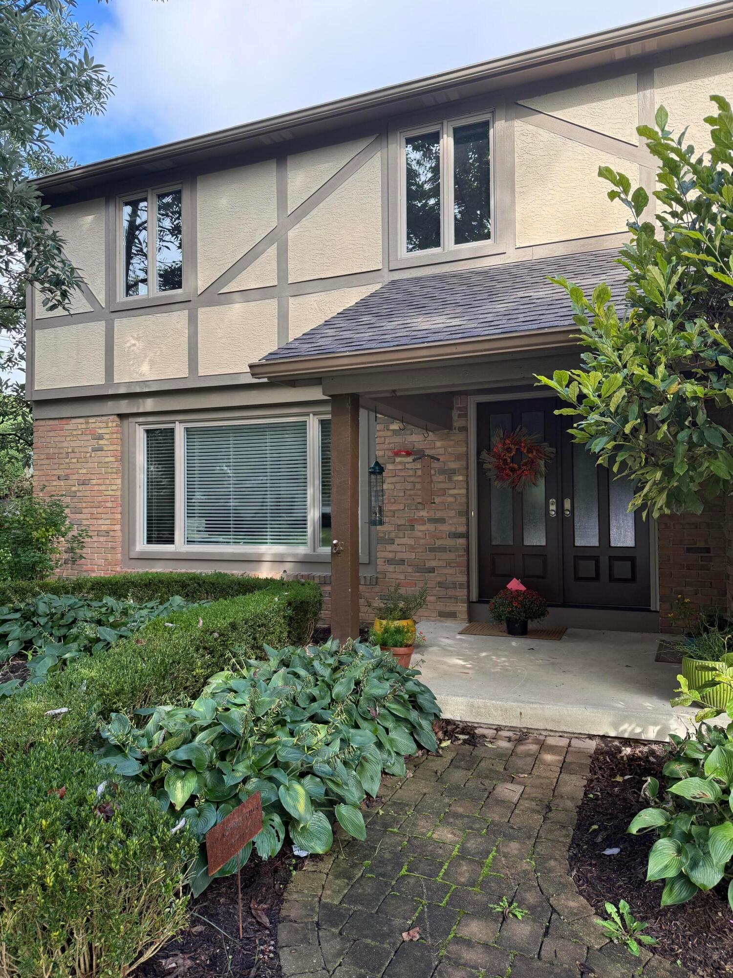 Two-story house with a brick lower level, dark double doors, and a landscaped paver walkway.