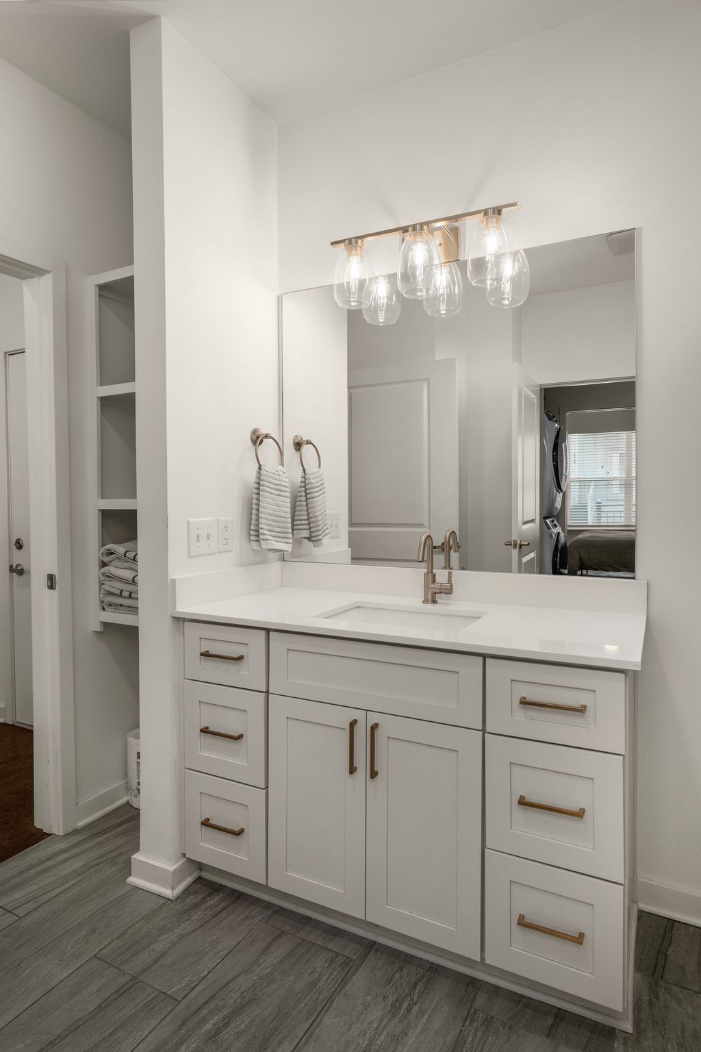 Bathroom vanity with white cabinetry, brass-tone fixtures, a large mirror, and open towel shelving.