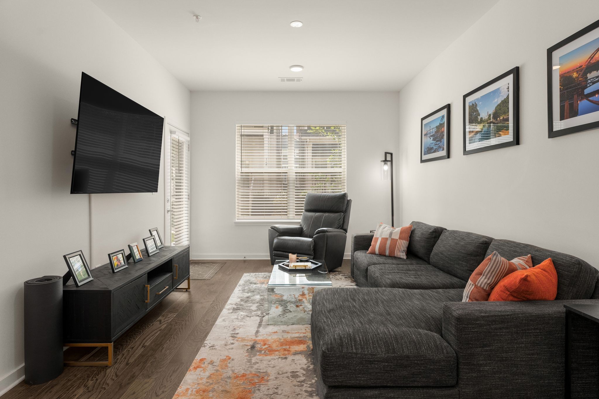 Living room with a dark sectional, orange pillows, leather recliner, and wall-mounted television.
