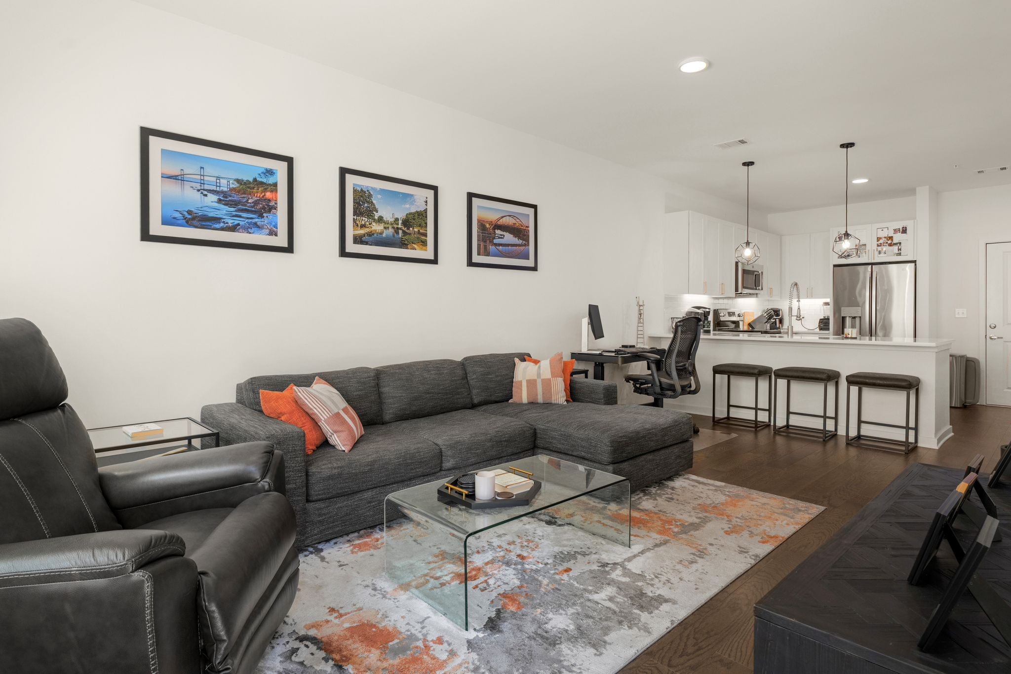 Open-plan living room with gray sectional, glass coffee table, and kitchen breakfast bar.
