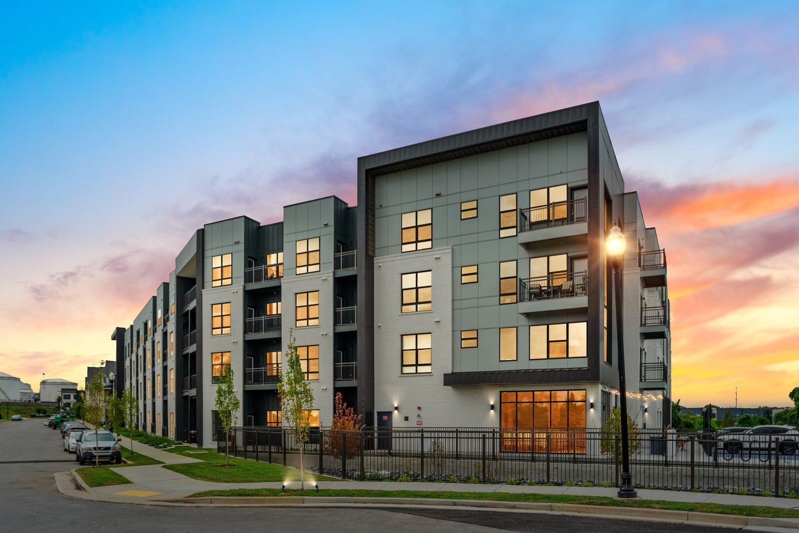 Modern apartment building with balconies and glowing windows beneath a colorful sunset sky.