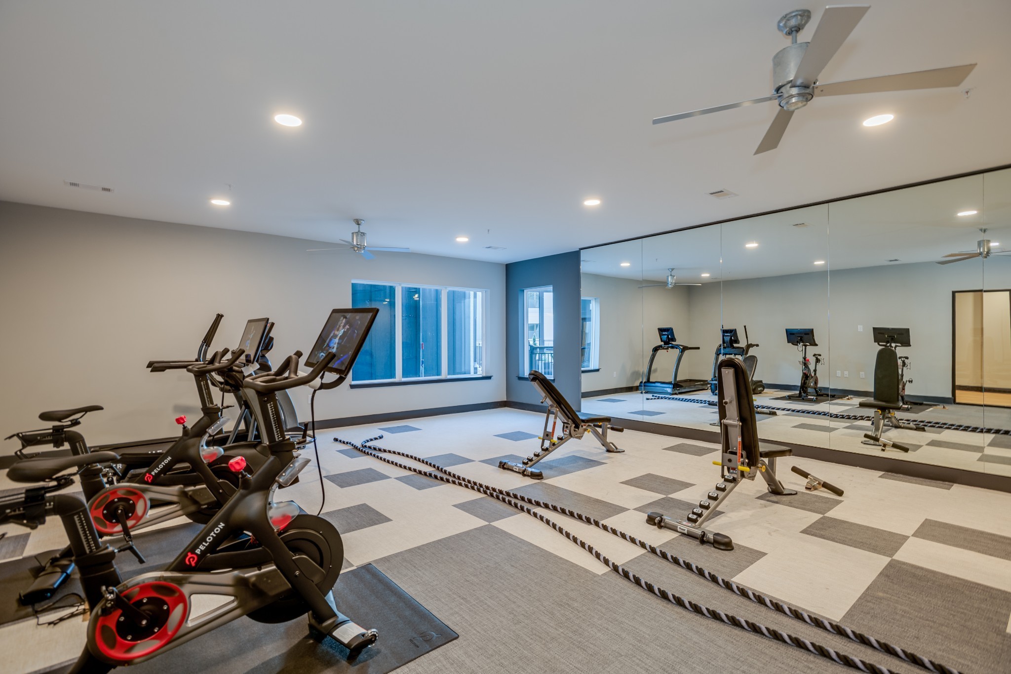 Fitness center with Peloton bikes, treadmills, exercise ropes, and a mirrored wall.