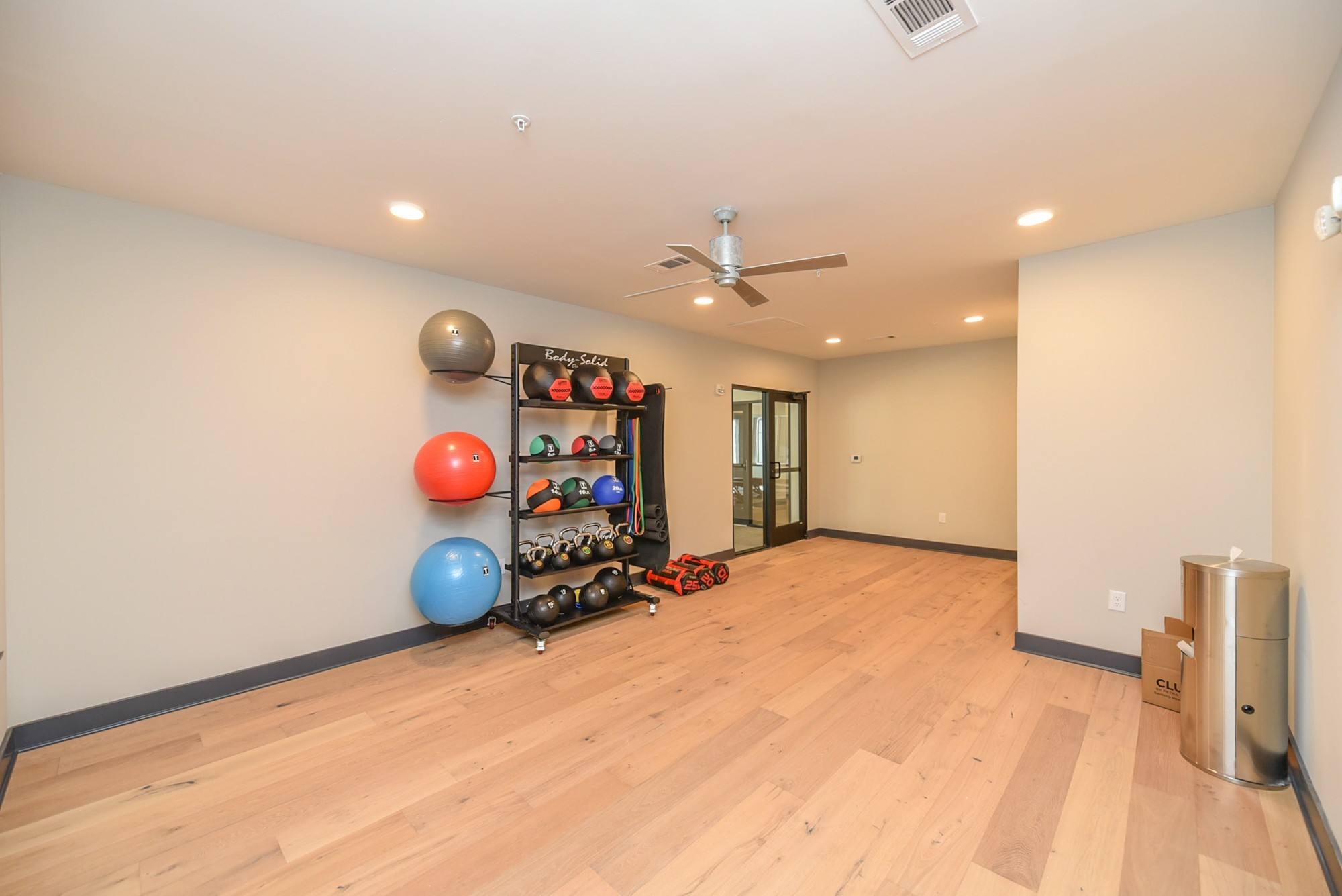 Fitness room with exercise balls and weights on a rack over light hardwood flooring.