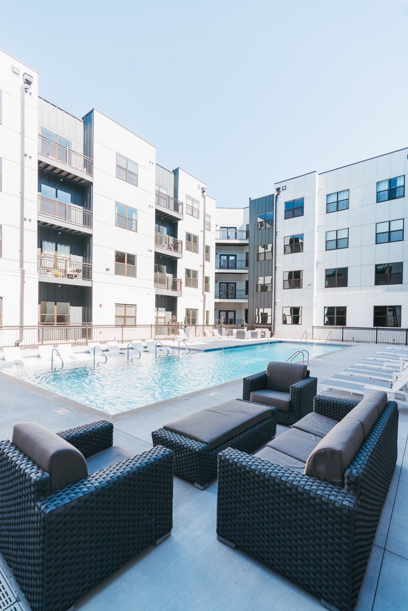 Apartment courtyard pool with wicker lounge seating and white sun loungers.