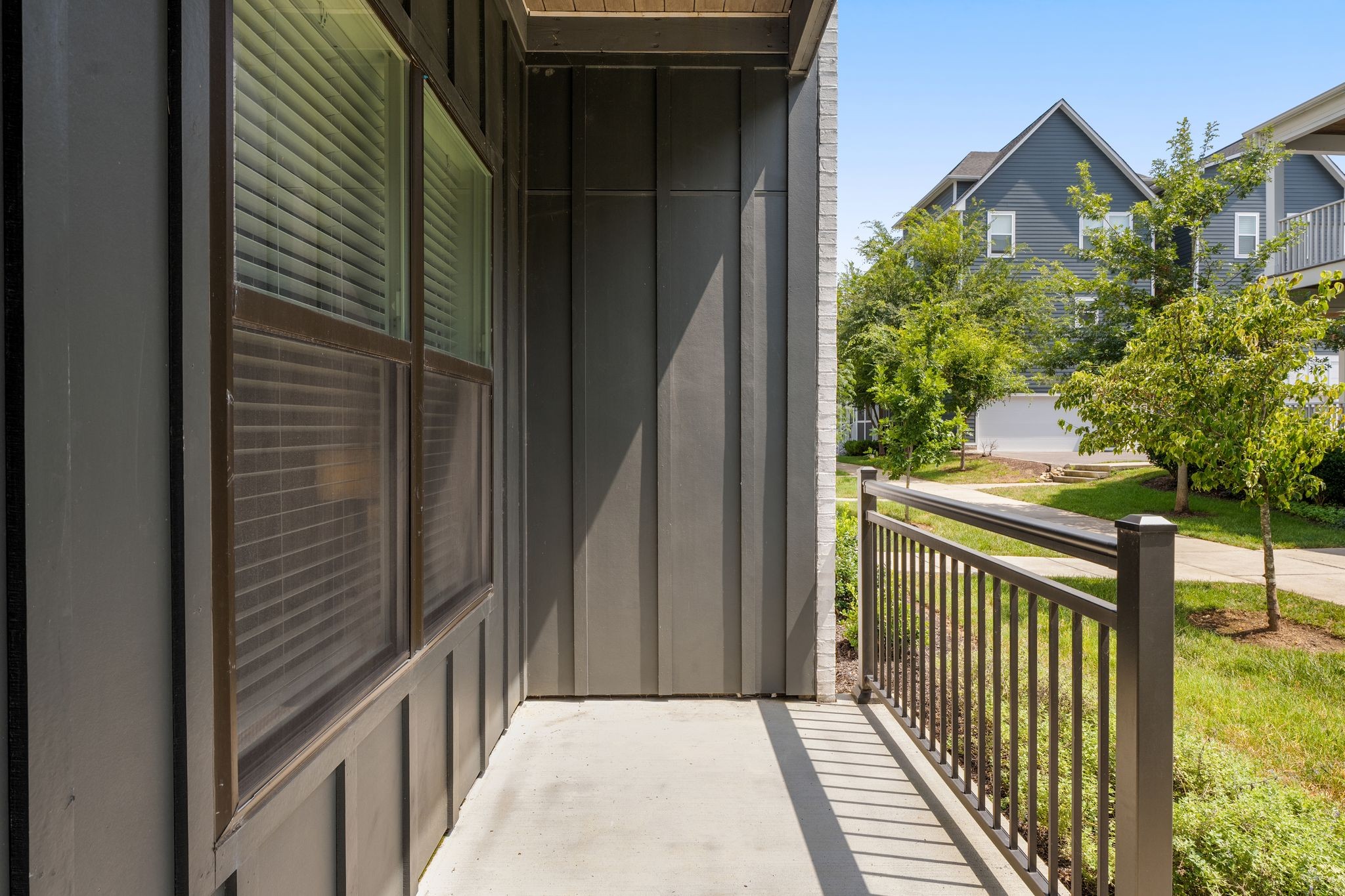 Covered porch with dark siding and metal railing overlooking trees and neighboring townhomes.