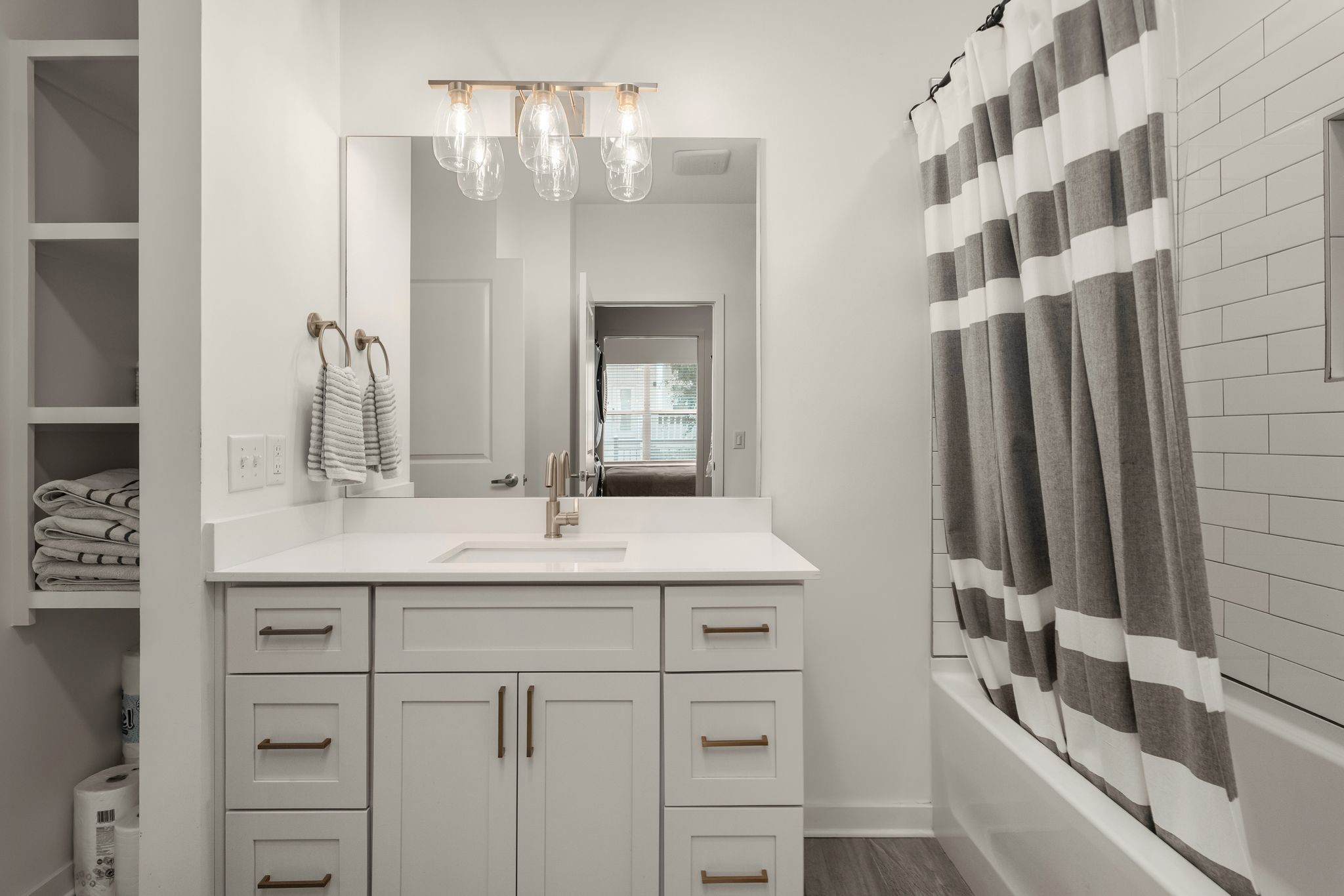 Bathroom with white vanity and sink, open towel shelves, and gray-and-white striped shower curtain.