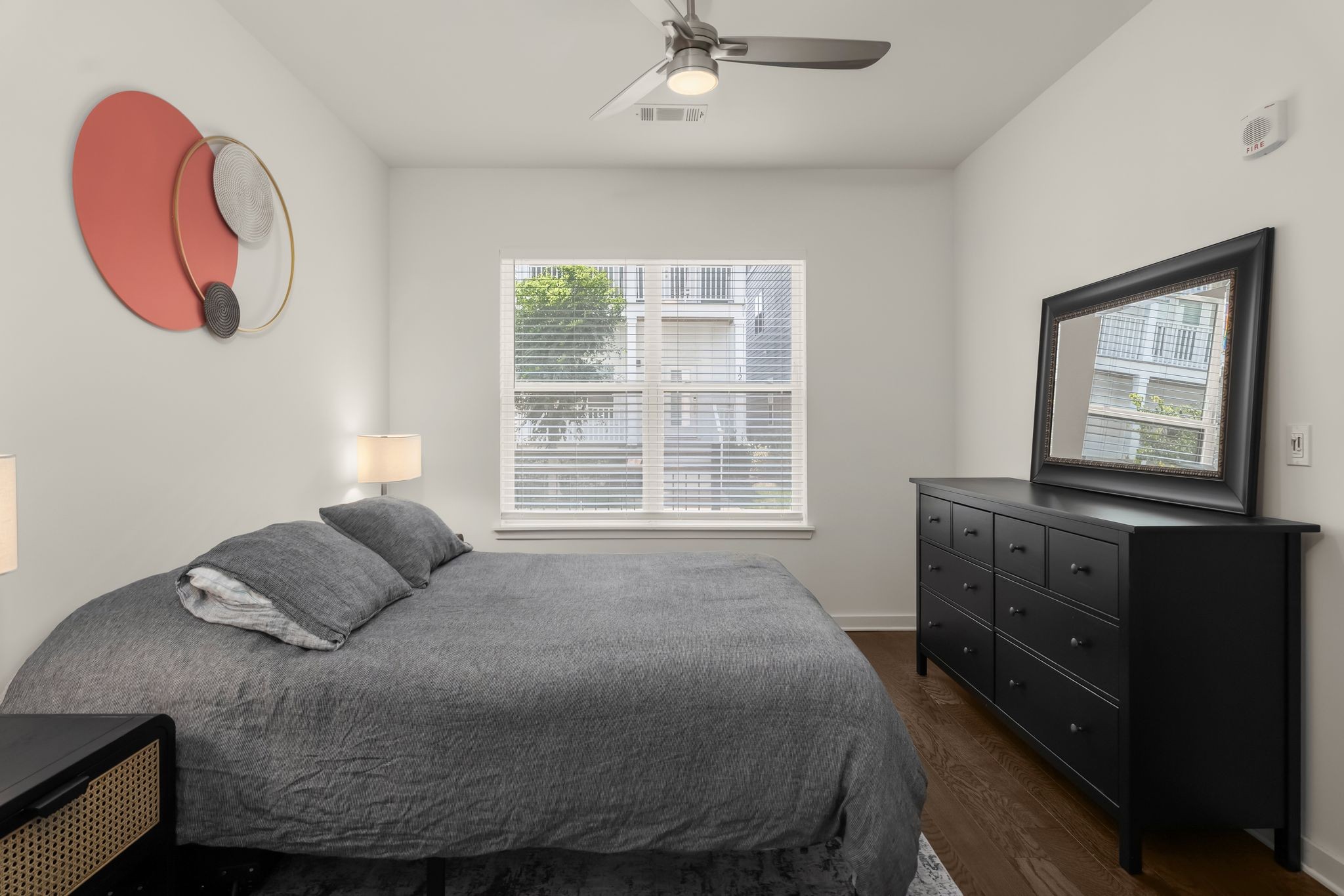 Bedroom with a gray bed, black dresser and mirror, and coral circular wall art.