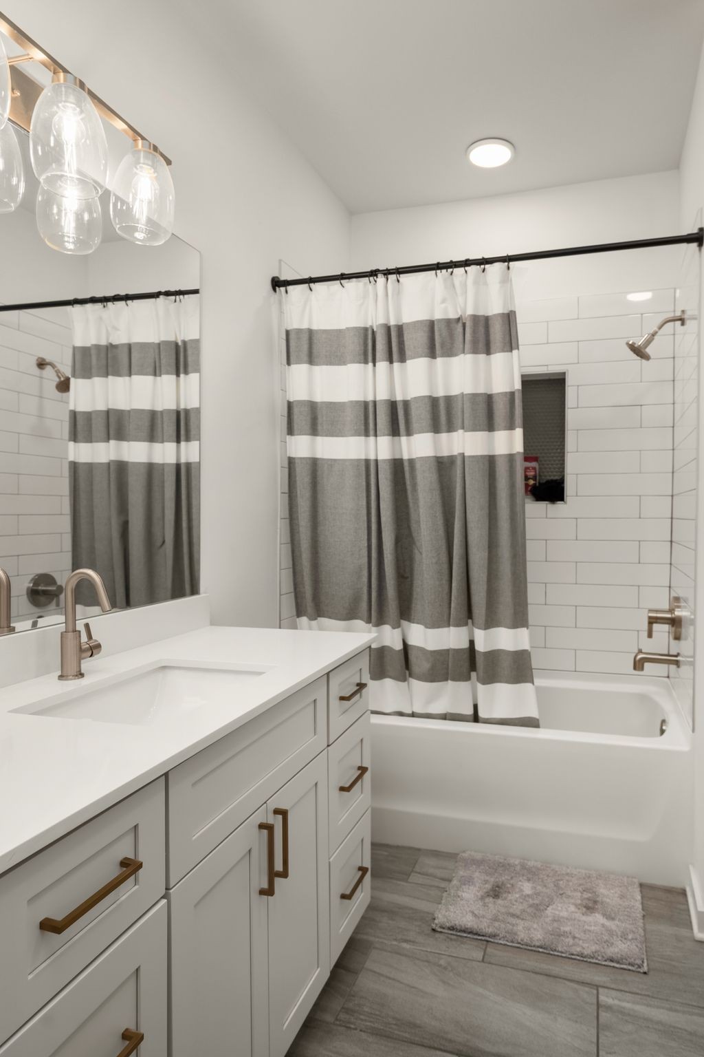 Bathroom with white vanity, brass hardware, striped shower curtain, and white subway tile around the tub.