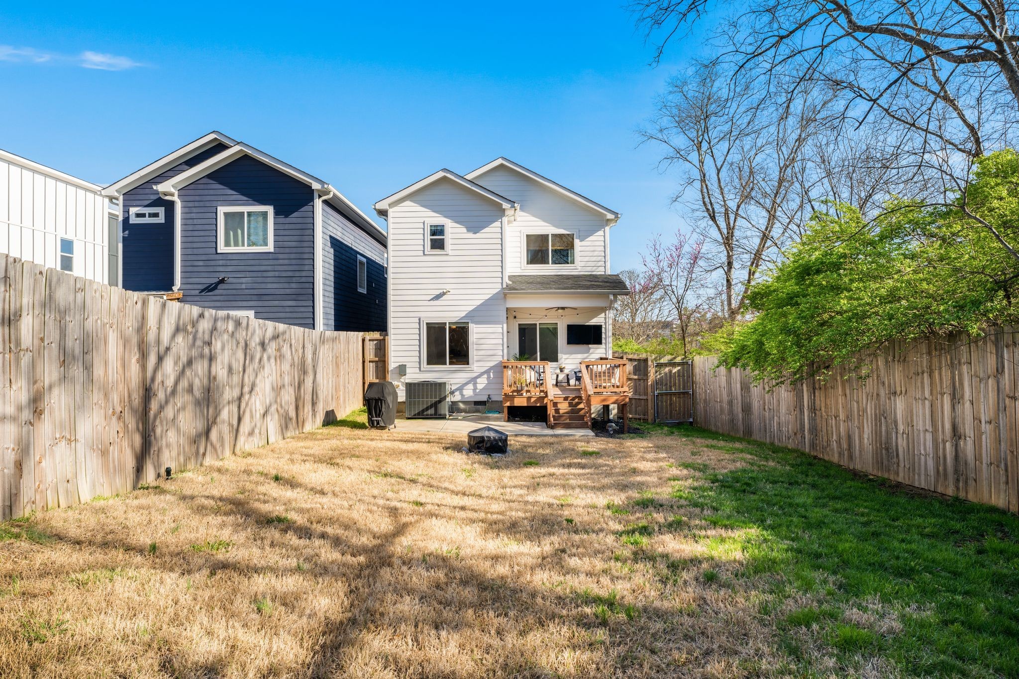 White two-story home with a raised wooden deck, seen across a fenced backyard.