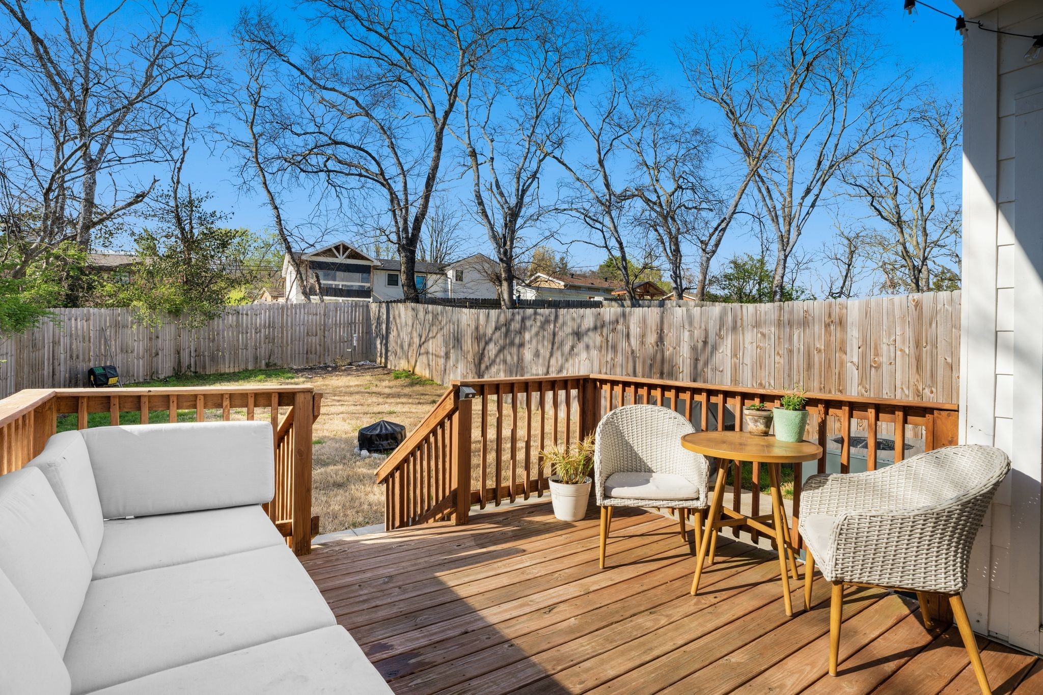 Backyard deck with white seating, wicker chairs, and a fenced yard beyond.