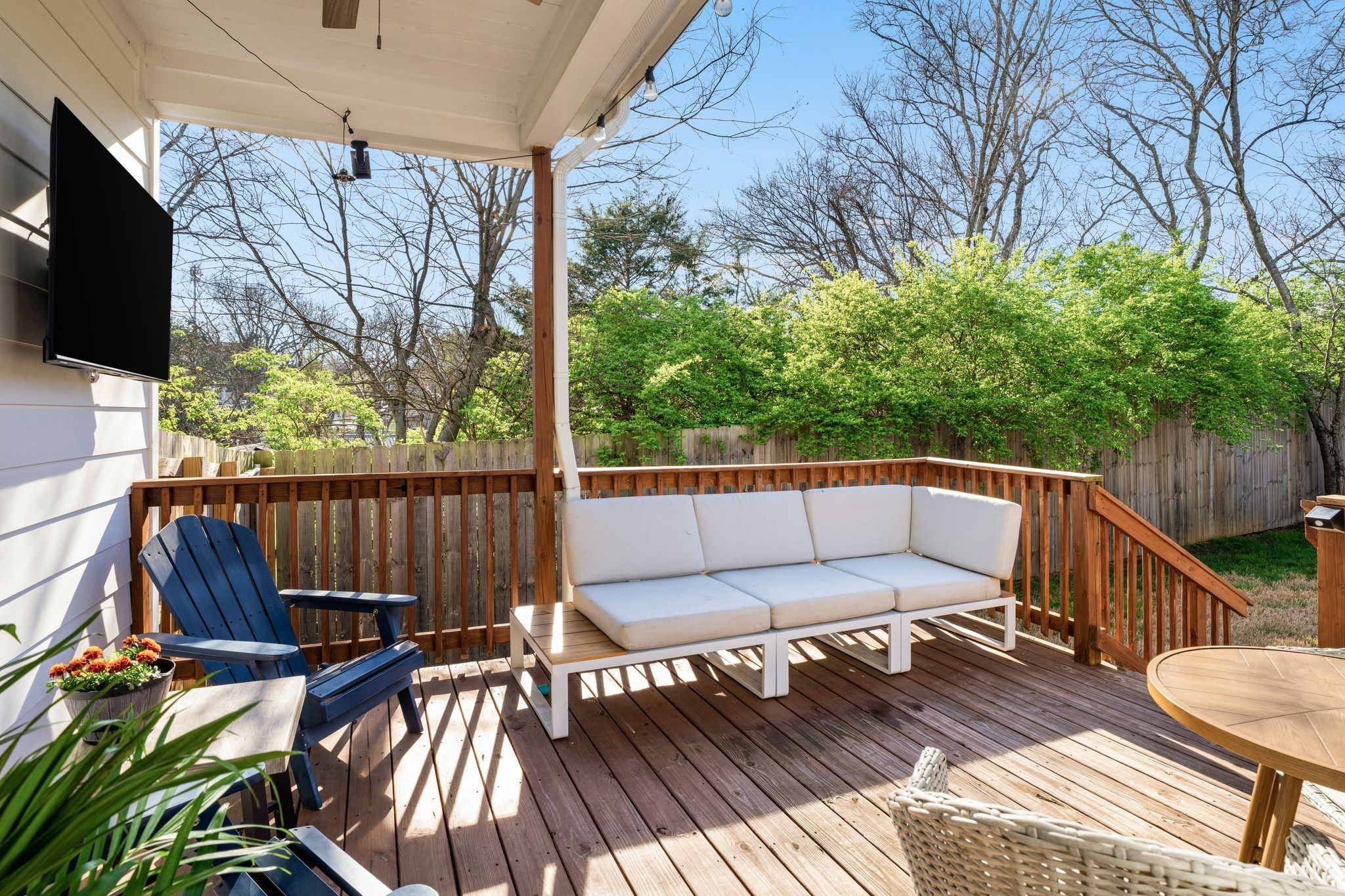 Furnished wooden deck with a covered seating area, outdoor sofa, Adirondack chair, and fenced green yard.