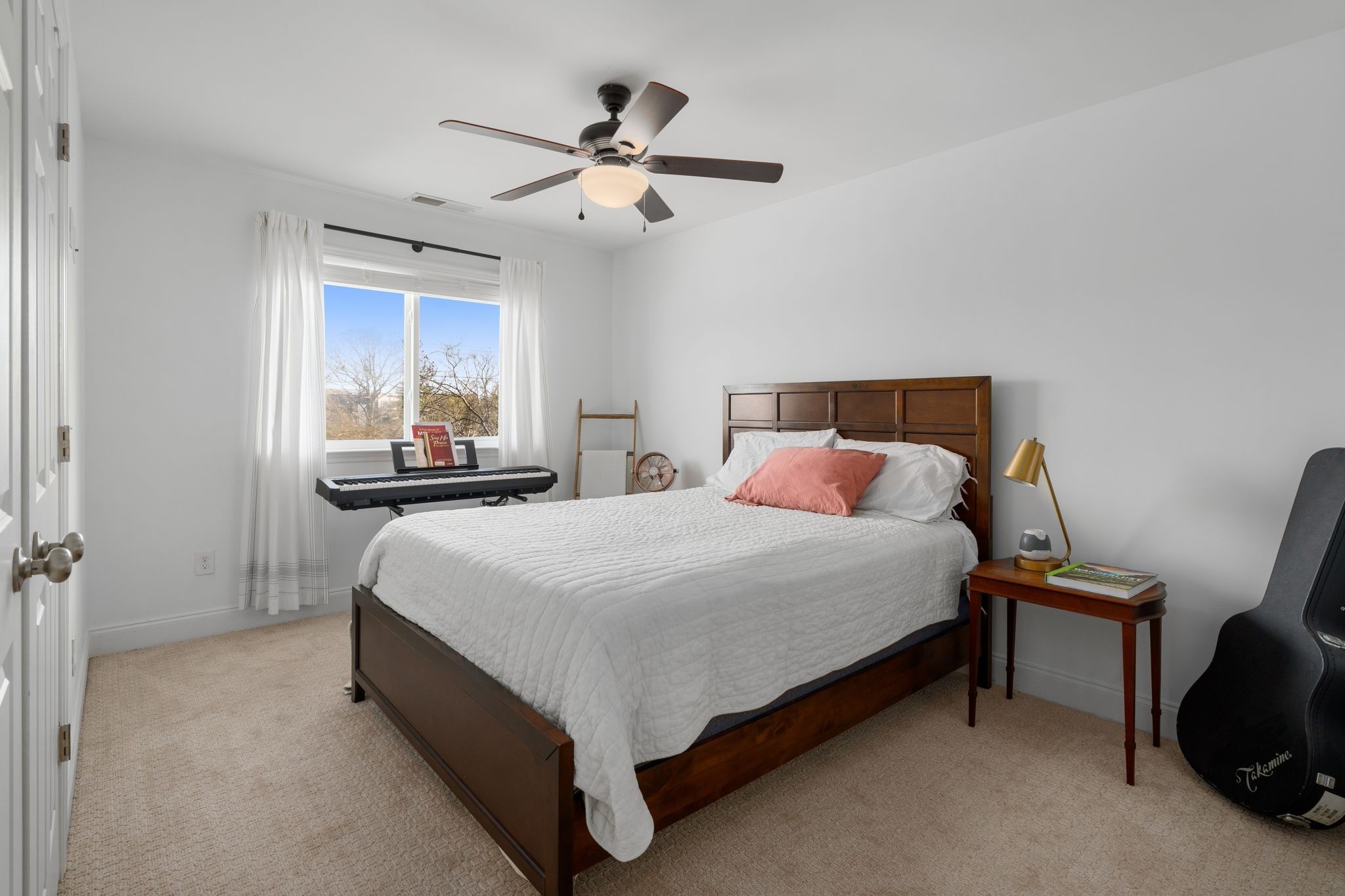 Furnished bedroom with a dark wood bed, coral accent pillow, keyboard, and guitar case.