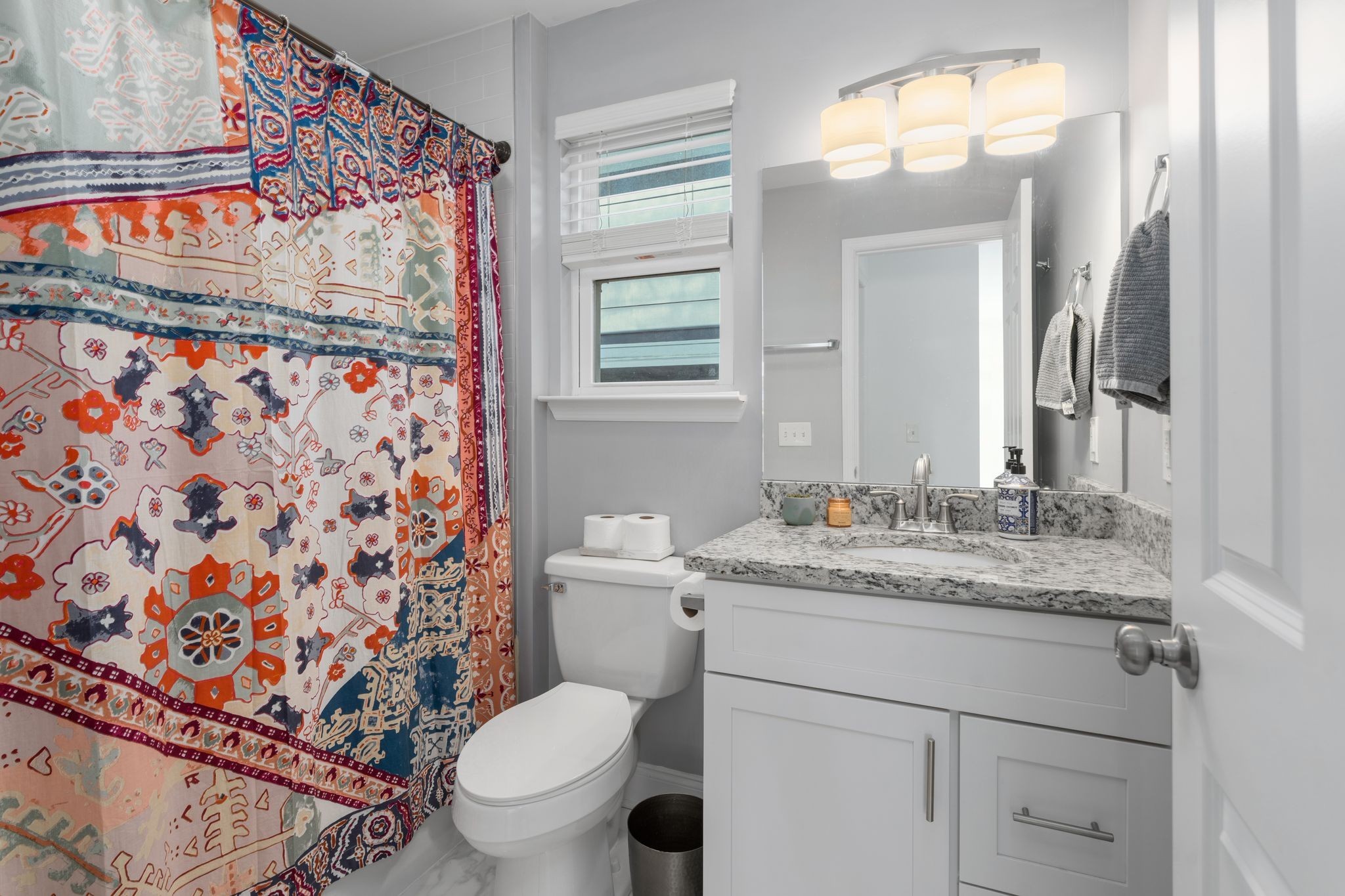 Bathroom with a colorful patterned shower curtain, stone vanity countertop, and large mirror.