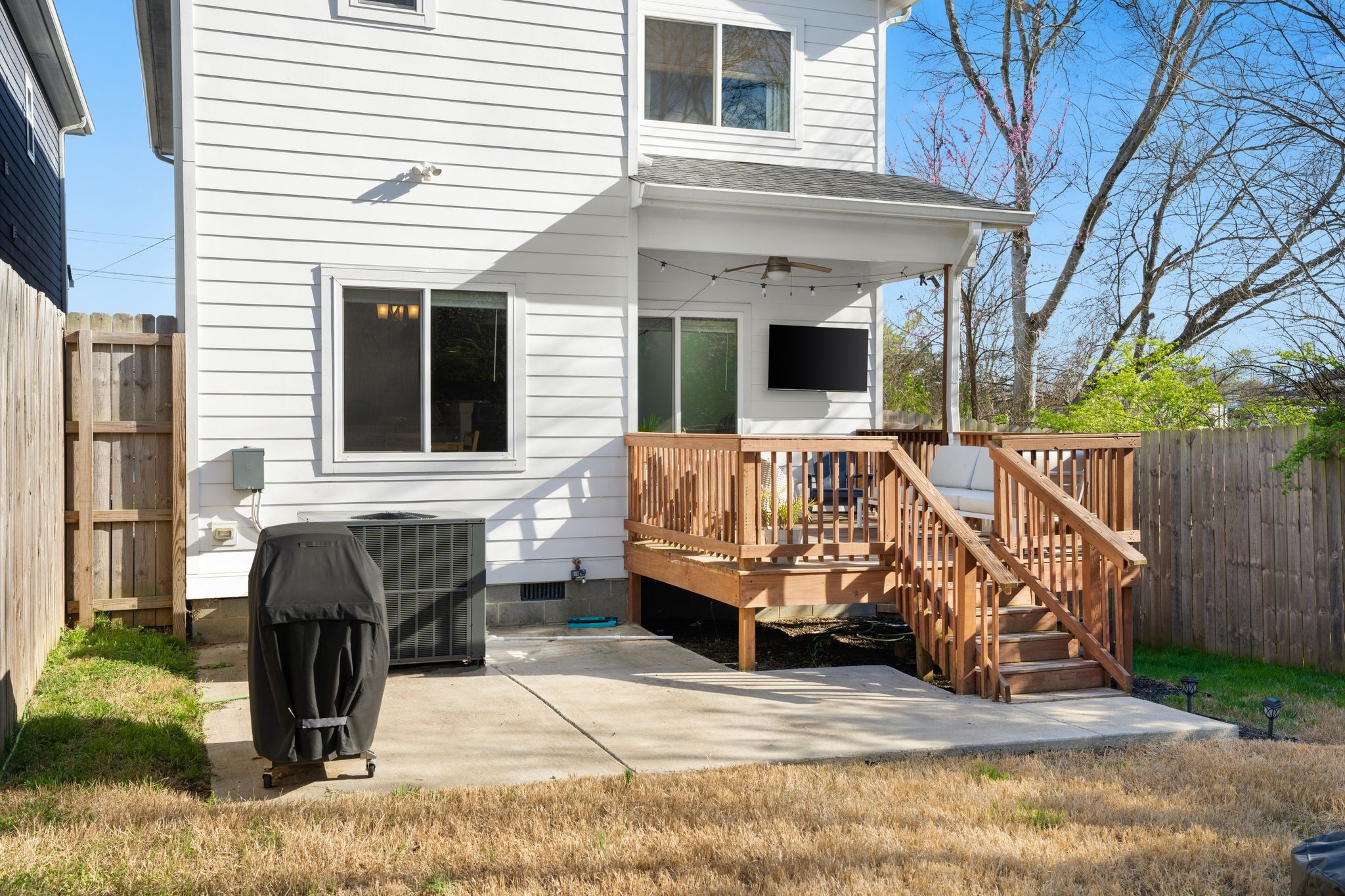 White home’s rear deck and covered patio with wooden stairs, outdoor seating, and a fenced yard.