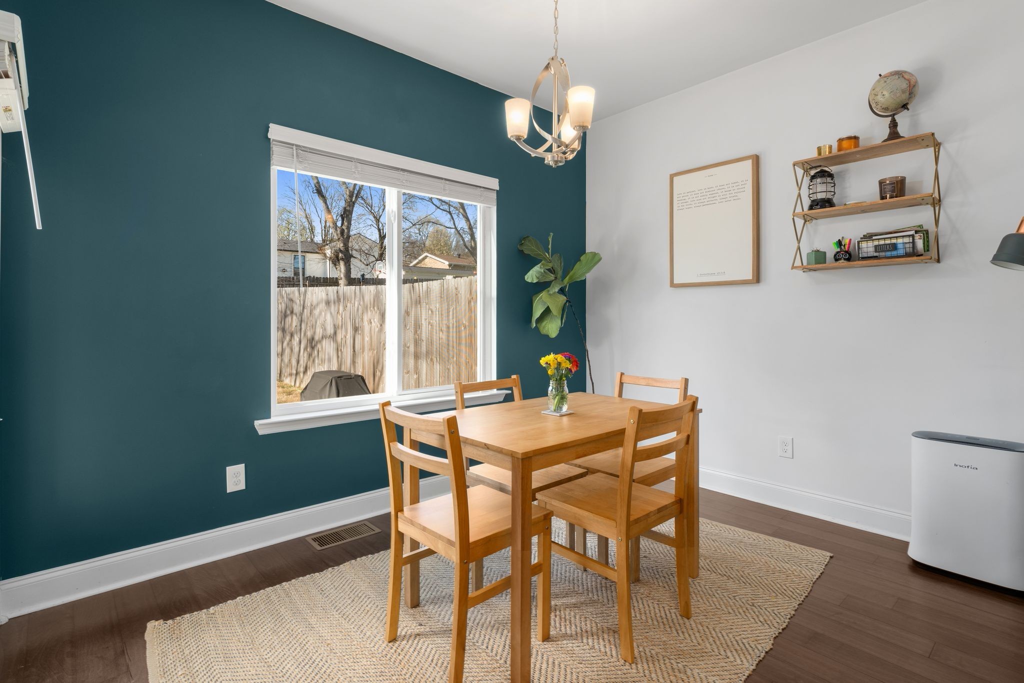 Dining area with a wooden table and chairs beside a large window and teal accent wall.