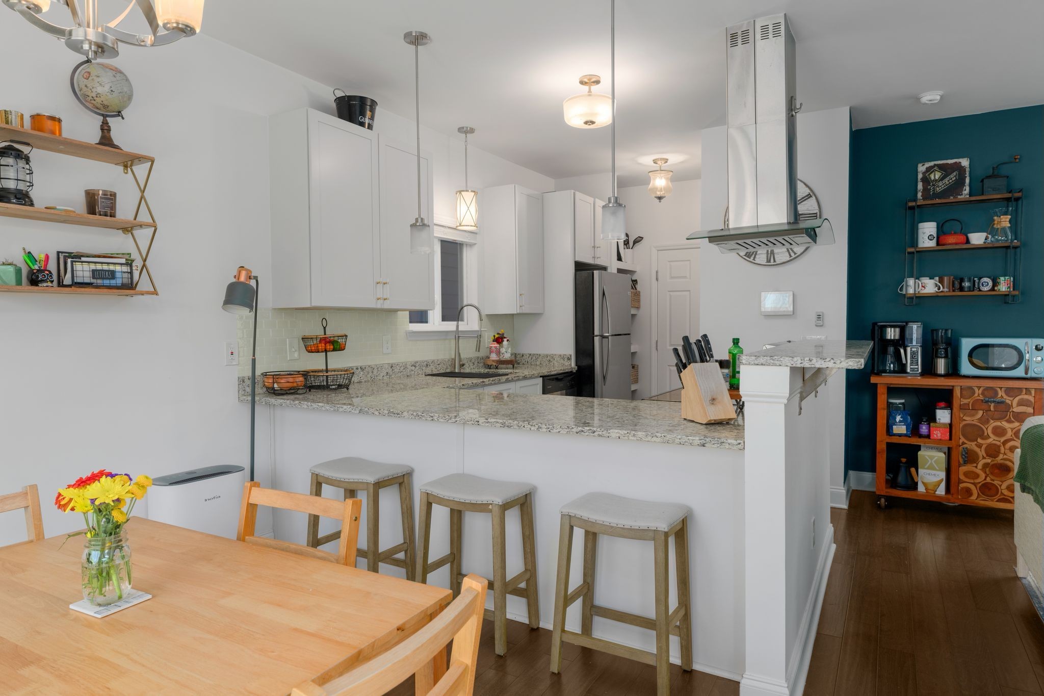 Kitchen with granite breakfast bar, three stools, white cabinets, and stainless steel appliances.