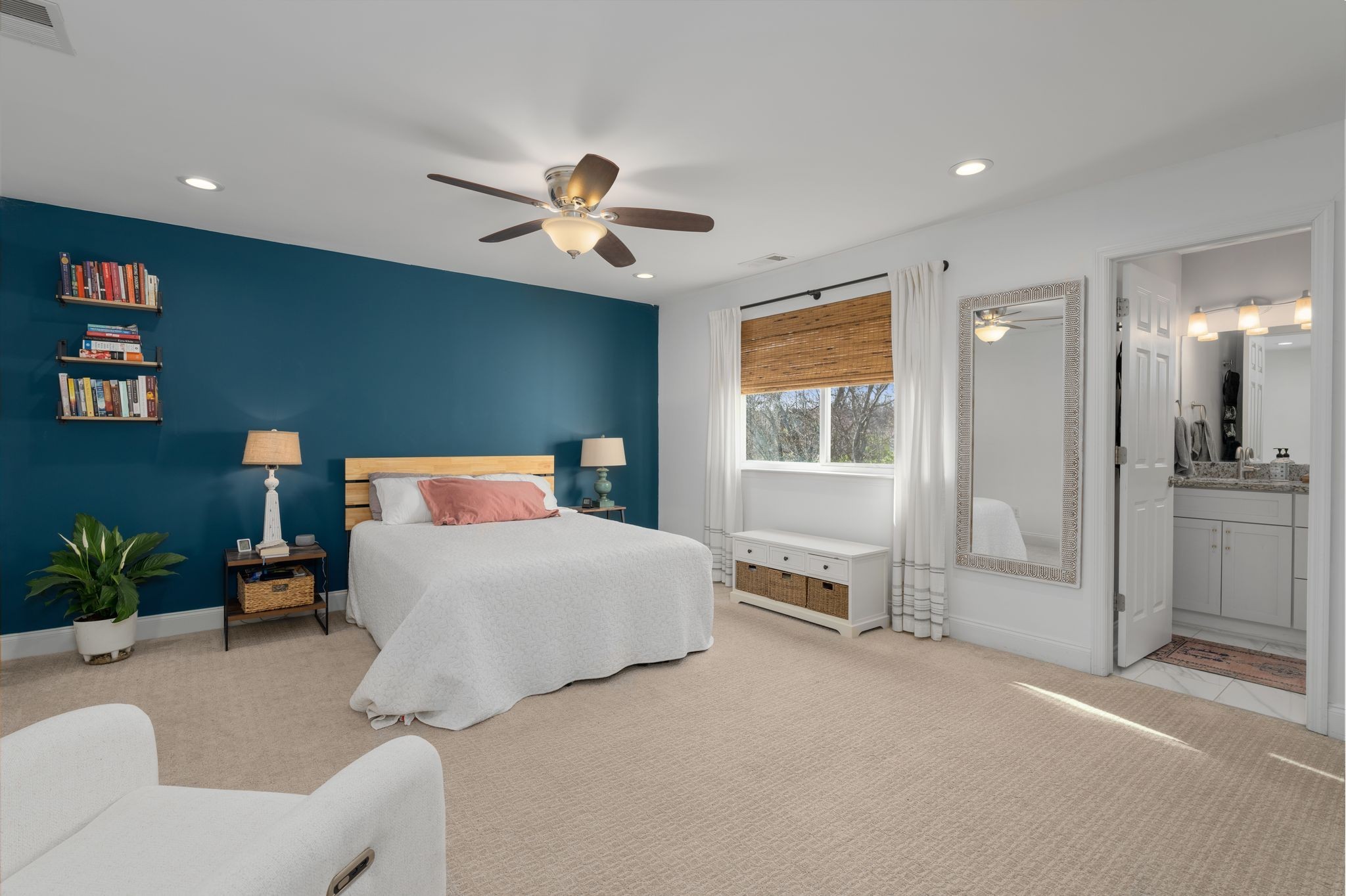 Furnished bedroom with a teal accent wall, white bed, and open doorway to the bathroom.