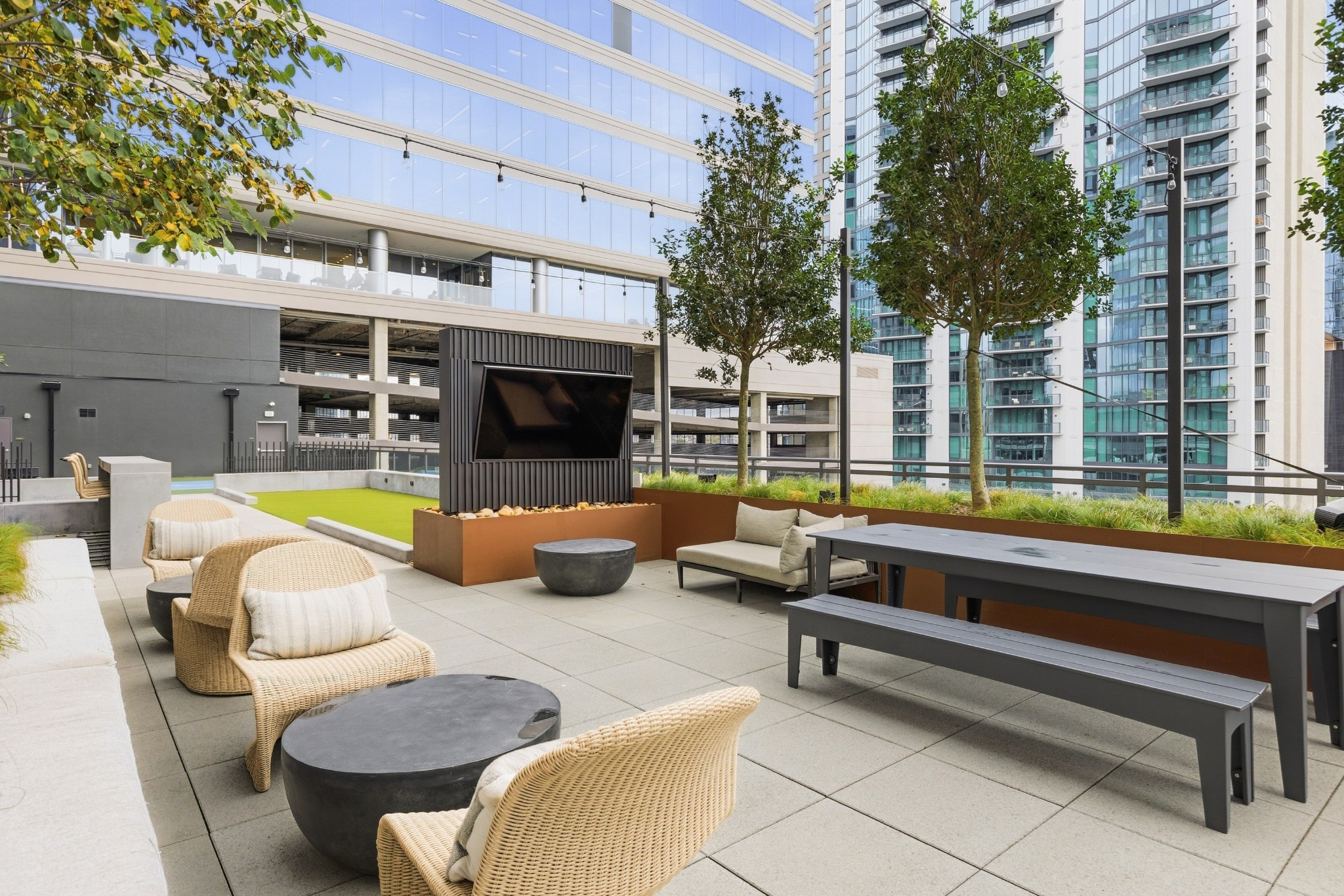 Rooftop terrace with wicker seating, a long dining table, raised planters, and an outdoor screen.