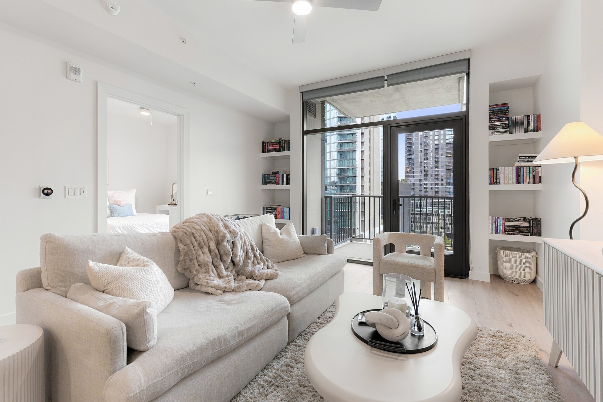 Bright condo living room with a cream sectional and balcony doors overlooking city buildings.