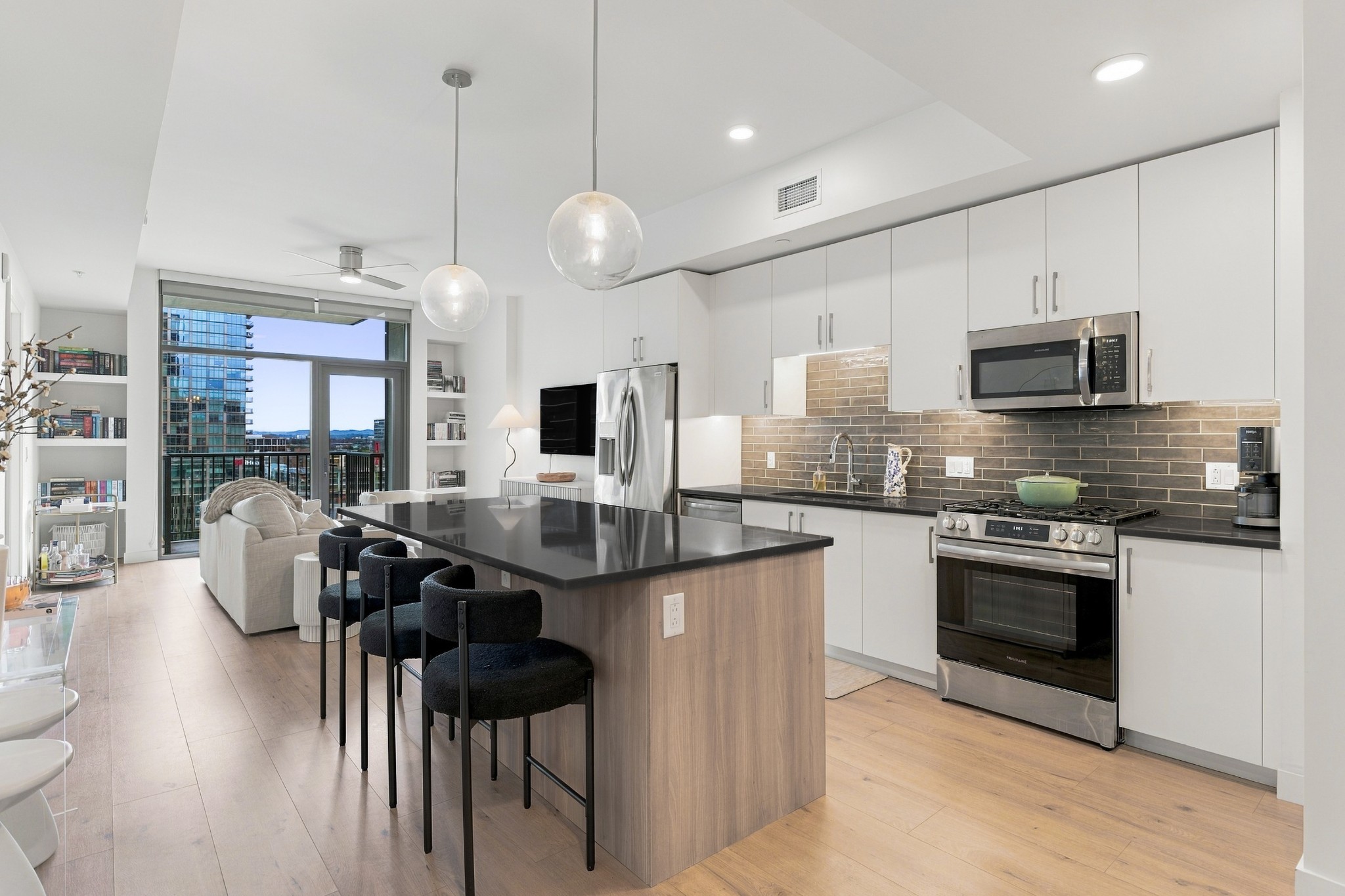 Open-plan condo kitchen with a large island and bar stools beside windows overlooking city buildings.