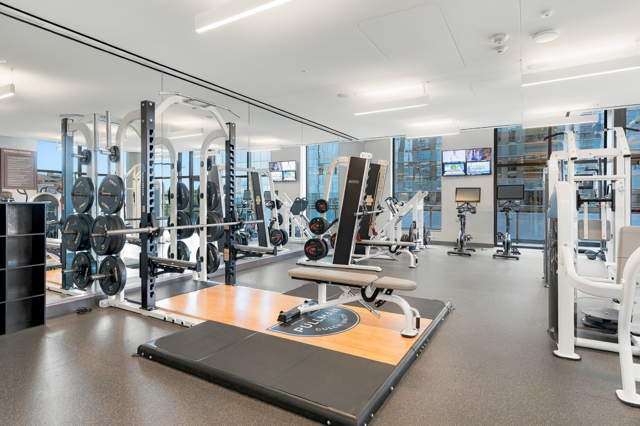 Residential fitness center with weight racks, strength machines, and floor-to-ceiling windows.