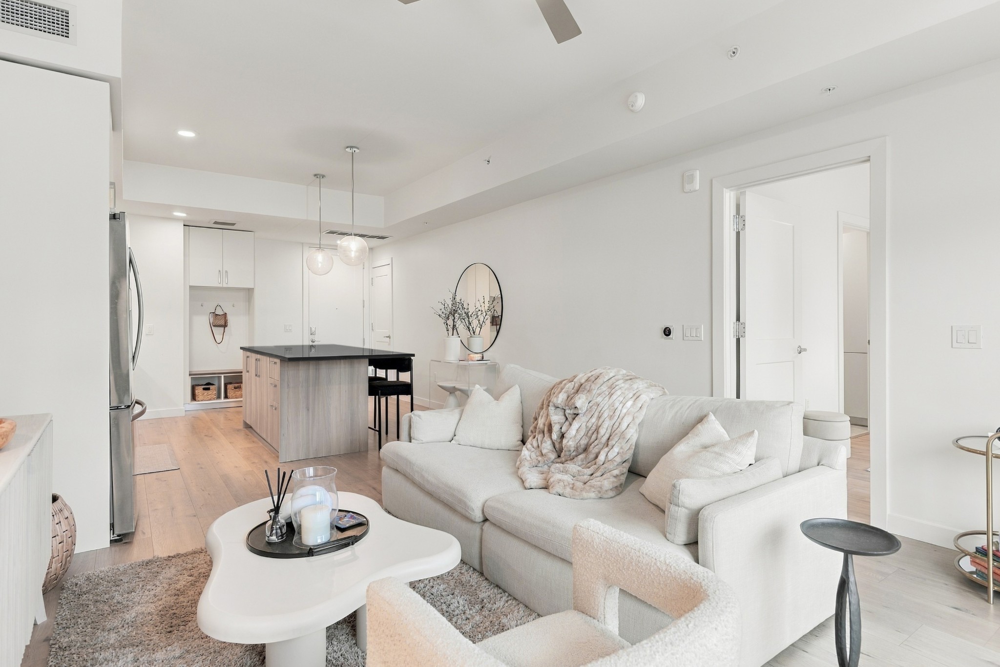 Open-plan condo living room with a white sectional, sculptural coffee table, and kitchen island.