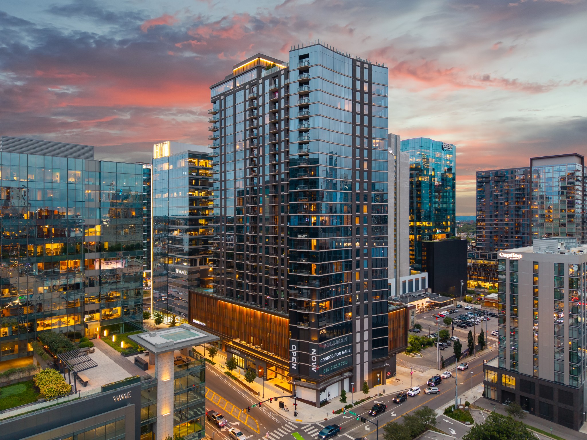 Modern high-rise condominium with glass façades and balconies among downtown towers at dusk.