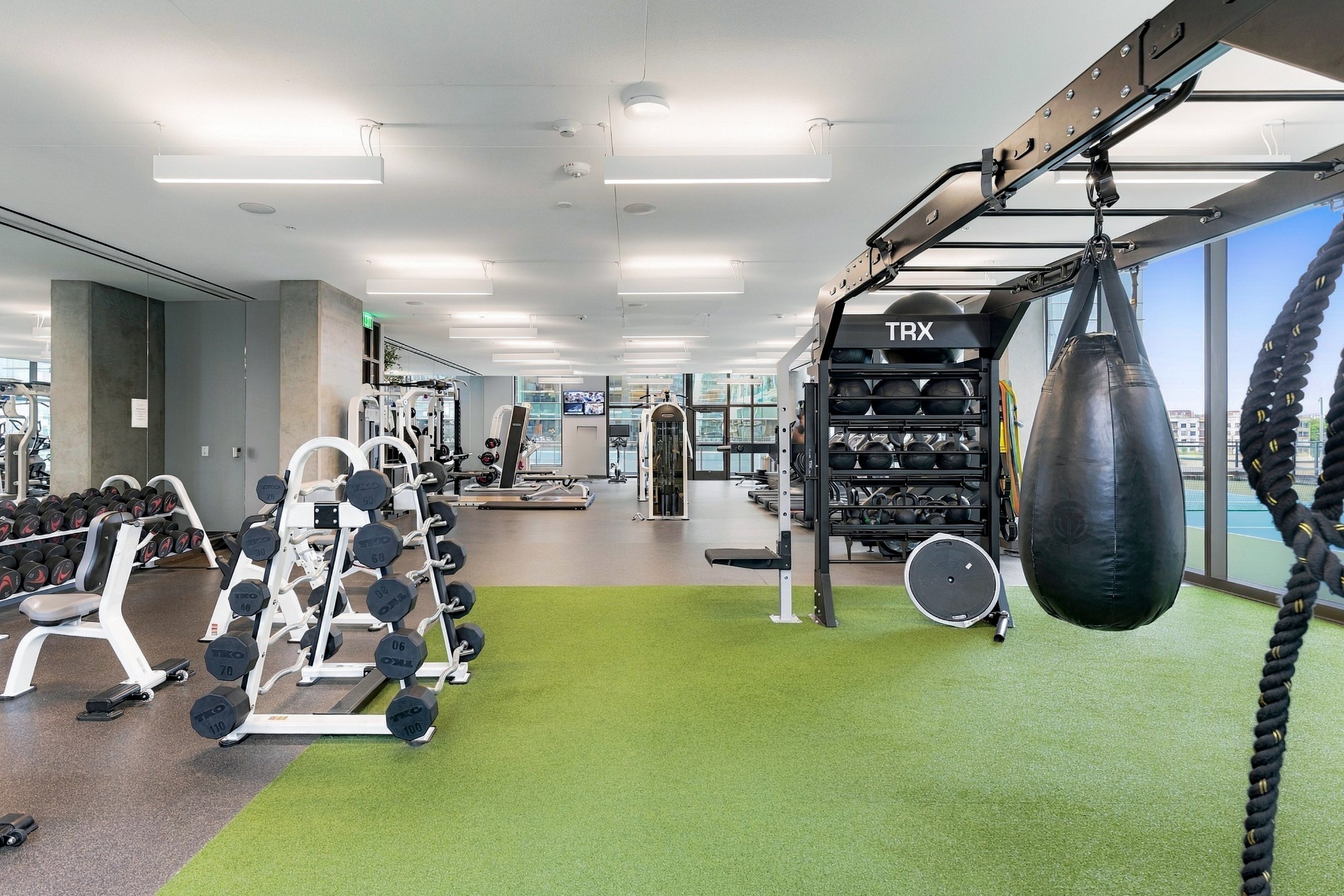 Building fitness center with dumbbells, green turf, TRX equipment, and a hanging punching bag.
