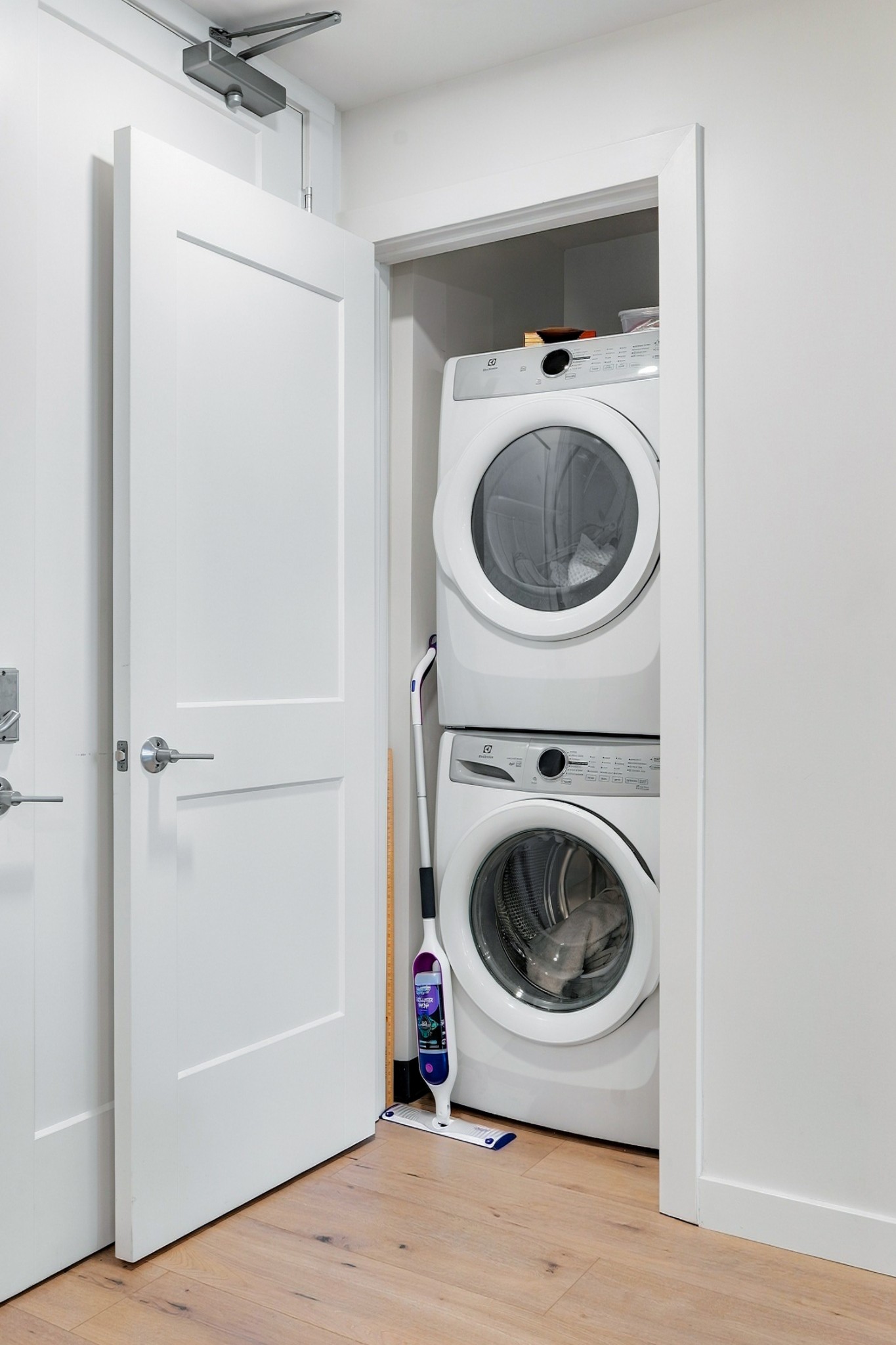 Laundry closet with stacked white front-loading washer and dryer behind an open door.