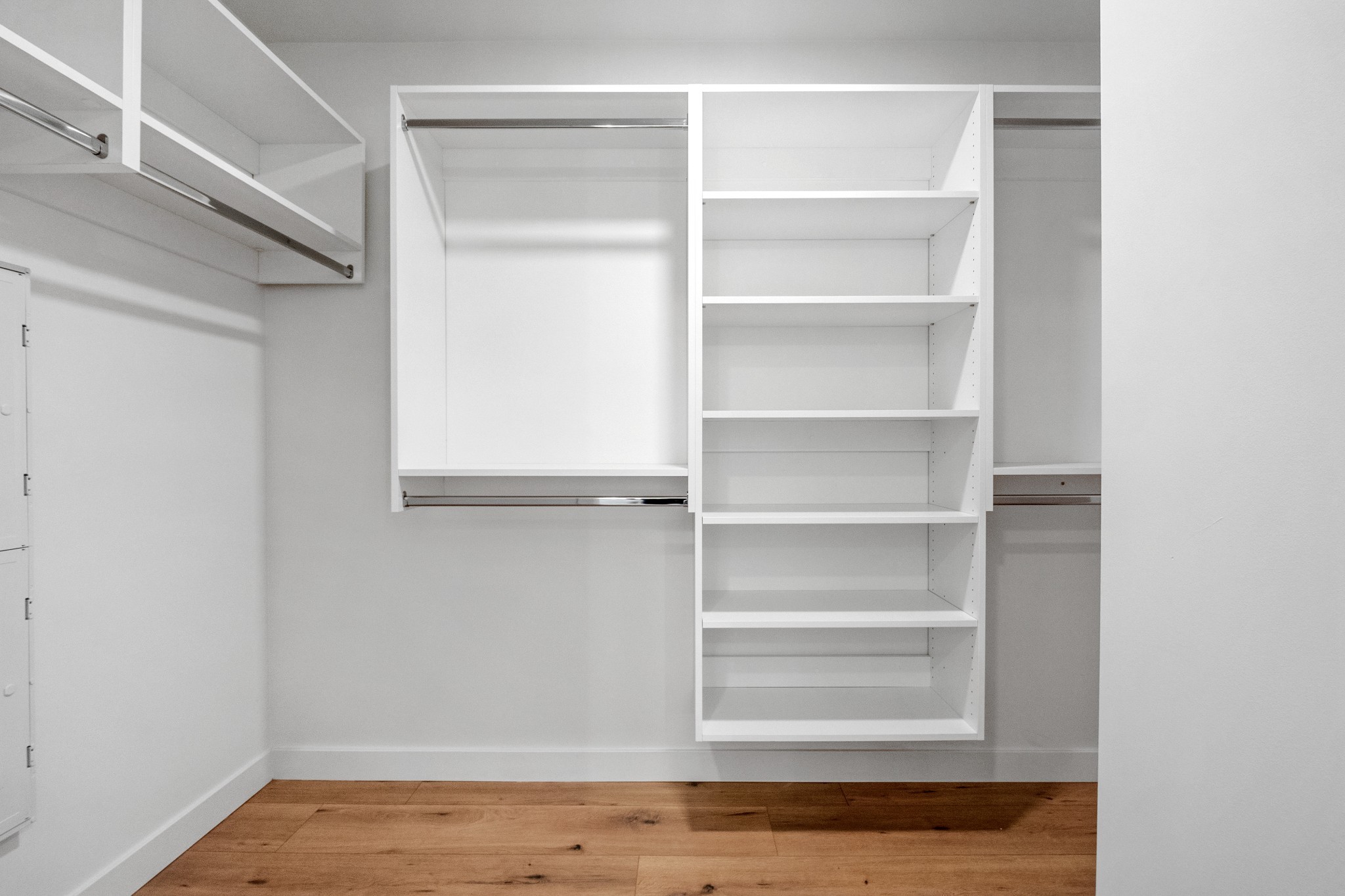 Walk-in closet with built-in white shelving, hanging rods, and wood flooring.
