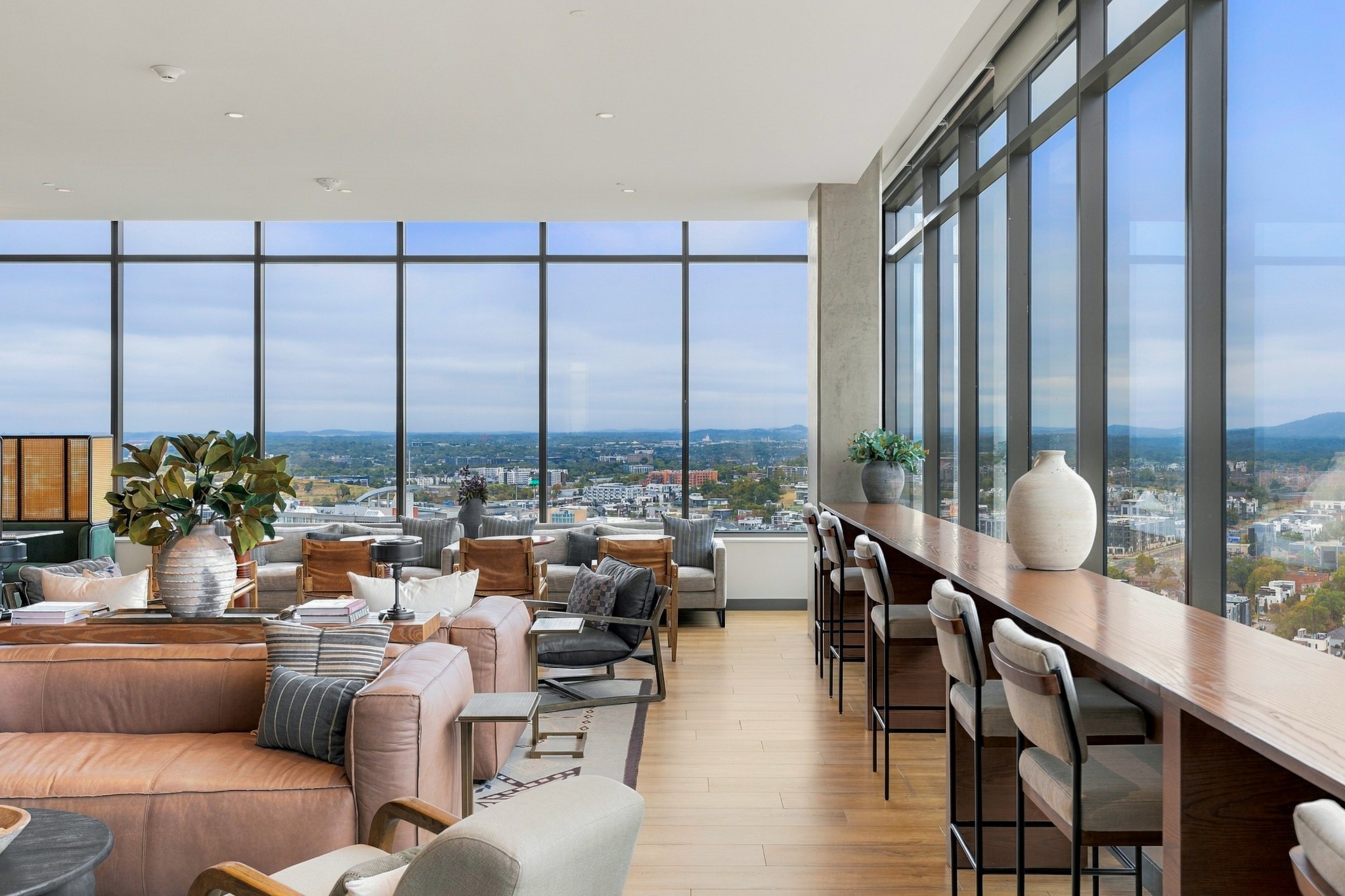 Furnished high-rise lounge with floor-to-ceiling windows, a long bar counter, and city views.
