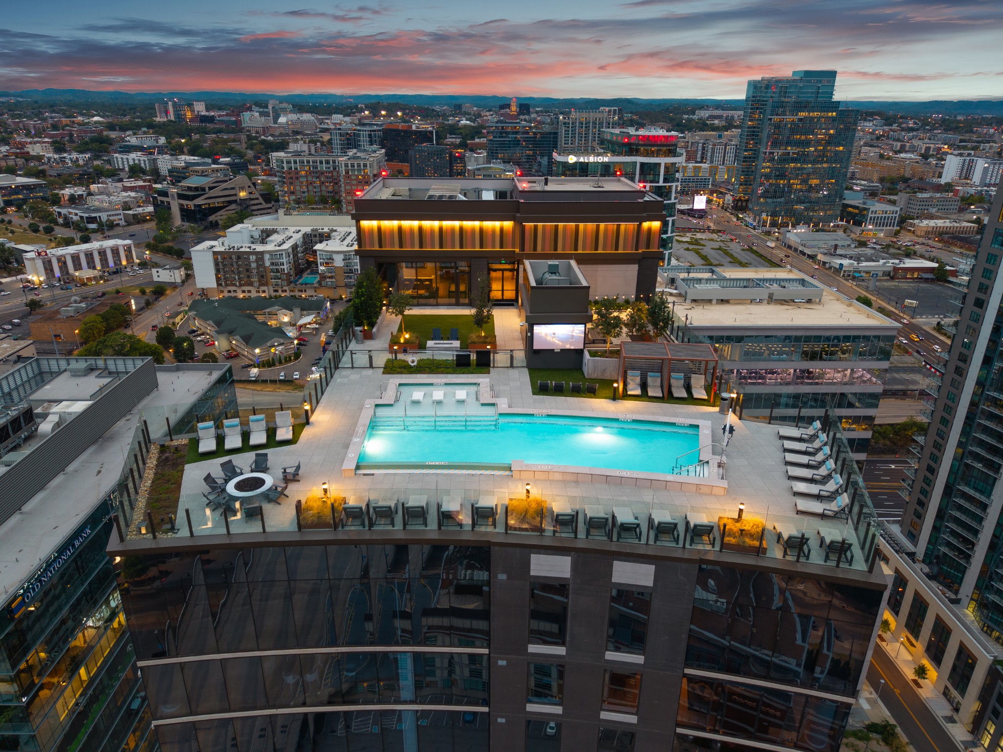 Rooftop pool and lounge deck overlooking downtown buildings at dusk.