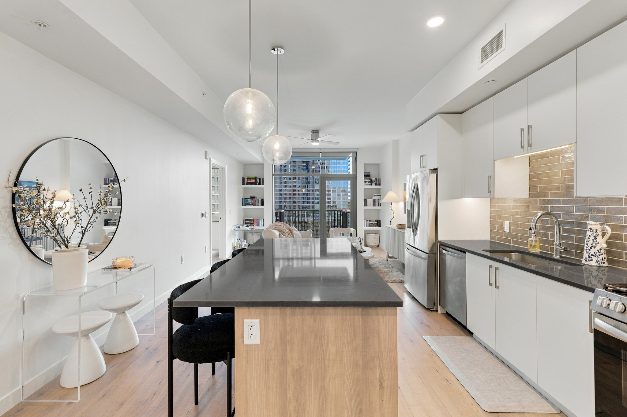 Furnished condo kitchen with a long island, white cabinetry, and city buildings visible through the window.